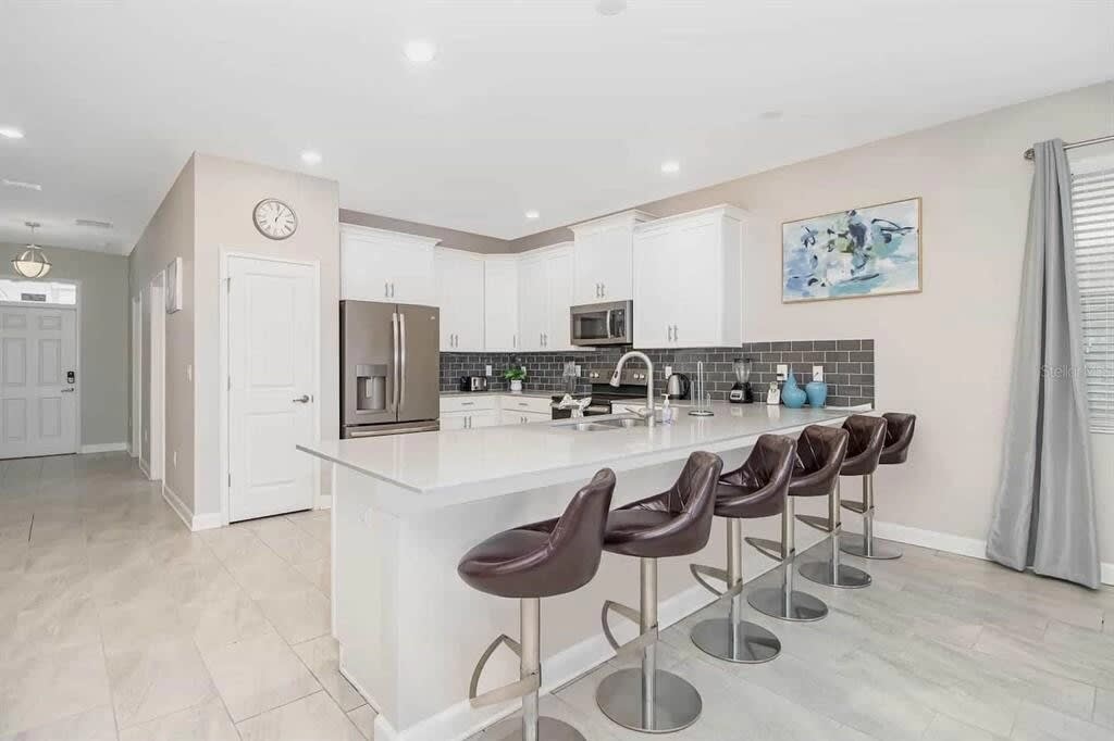 Bright private kitchen with a spacious island, four leather bar stools, stainless-steel appliances, and a stylish gray tile backsplash for group meals and gatherings.