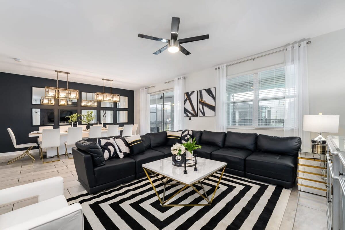 Open-plan living and dining room with a spacious black leather sectional, marble-top coffee table, bold geometric rug, and seating for group meals.