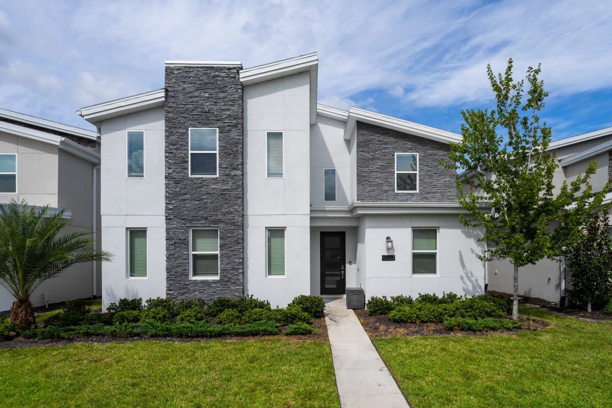 Modern villa exterior with a dramatic stacked-stone facade, landscaped lawn, and a welcoming walkway leading to the private entrance.