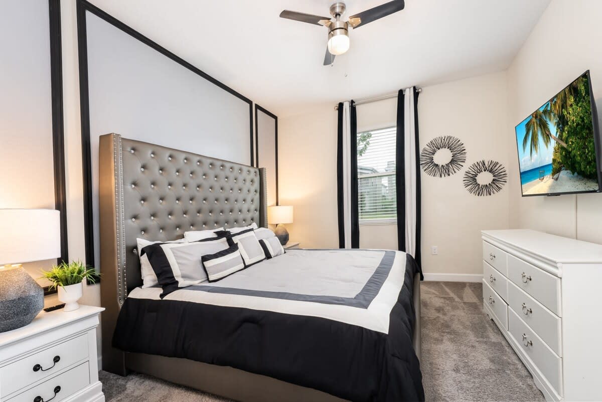Private king bedroom with a tufted gray headboard, crisp black-and-white bedding, and a wall-mounted TV overlooking the room.