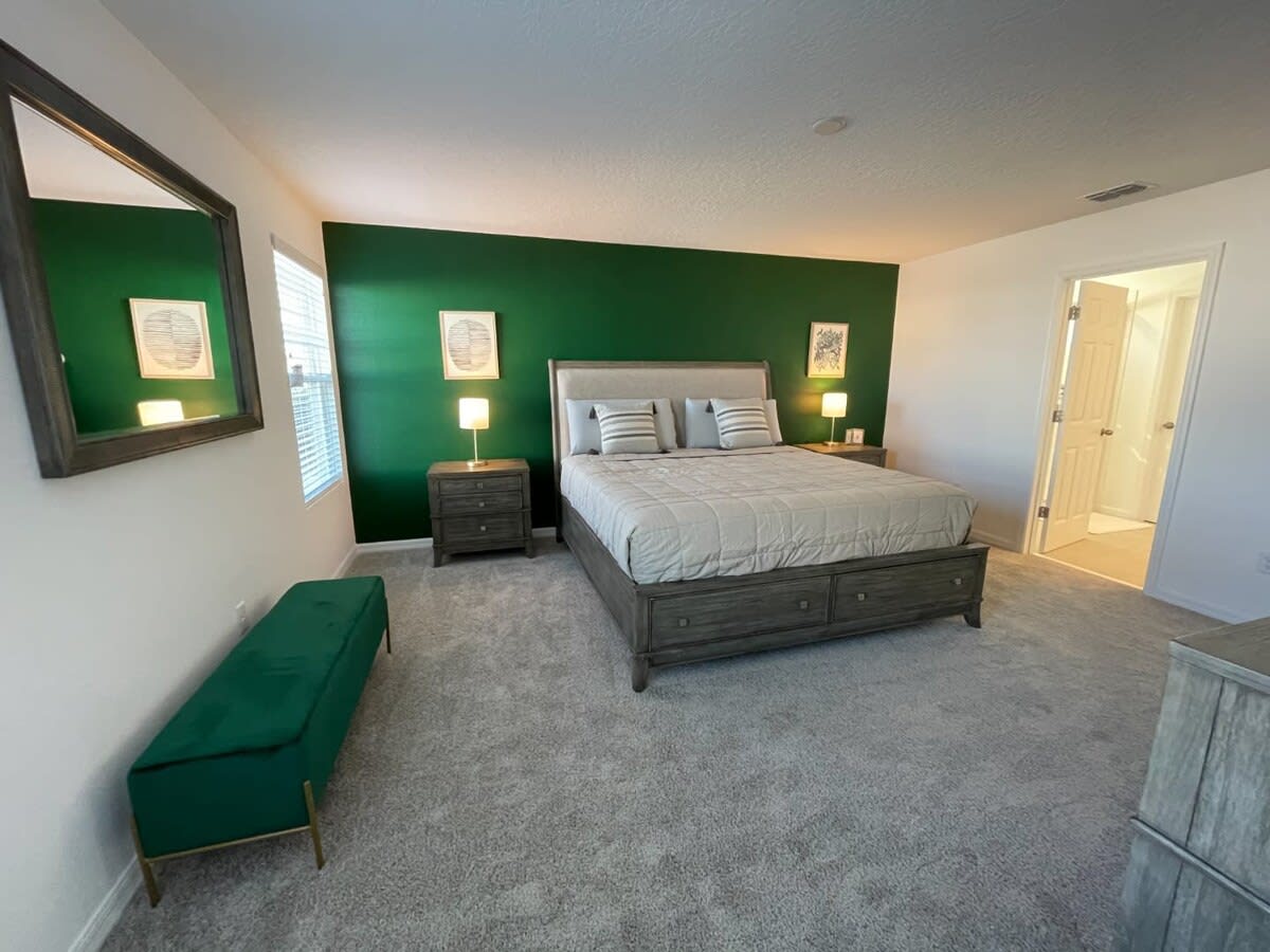 Relax in this elegant bedroom with a king-size bed and vibrant green accent wall, offering a serene retreat.