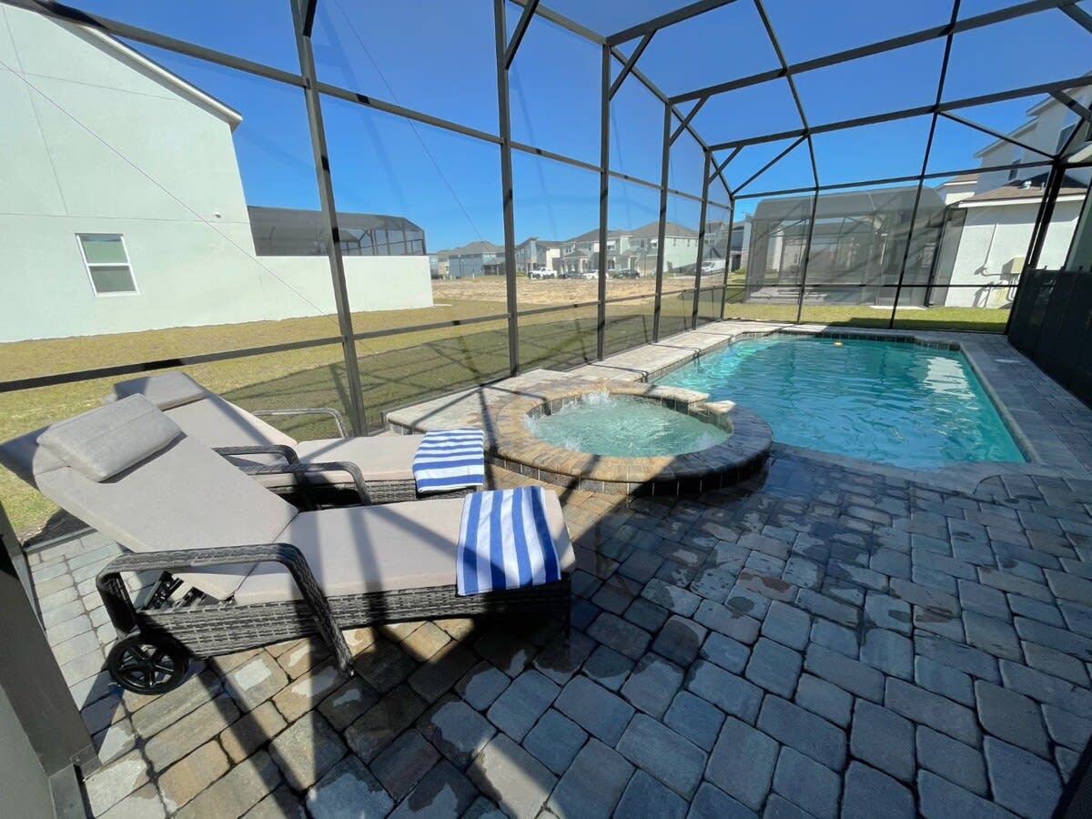 Private screened pool and bubbling spa with cushioned loungers, striped towels, and open-sky views for relaxing outdoors.