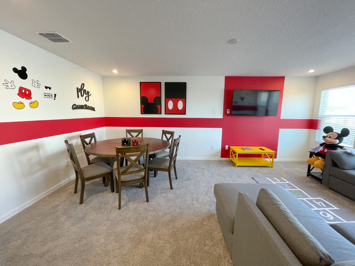 Enjoy family fun in this Mickey Mouse-themed game room with a game table, TV, and cozy seating, perfect for entertainment.