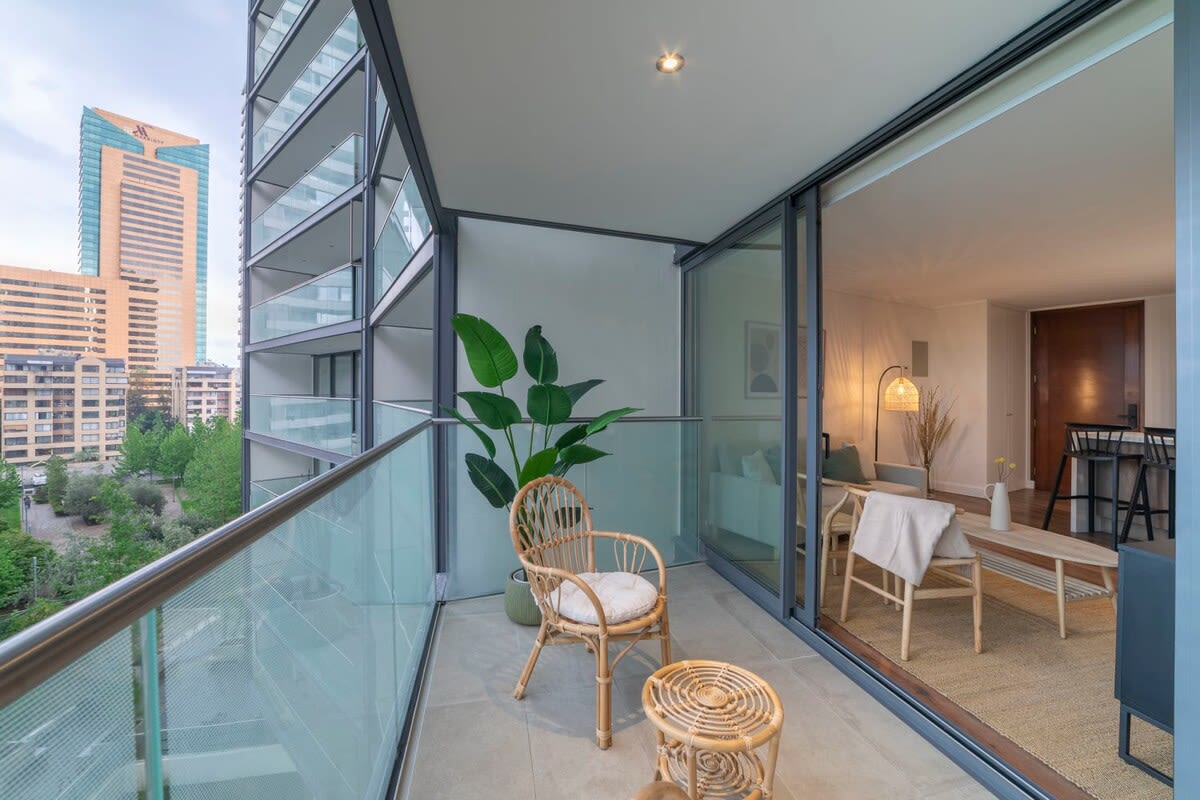 Enjoy stunning city views from your private balcony, complete with cozy wicker seating and easy access to a stylish living space.