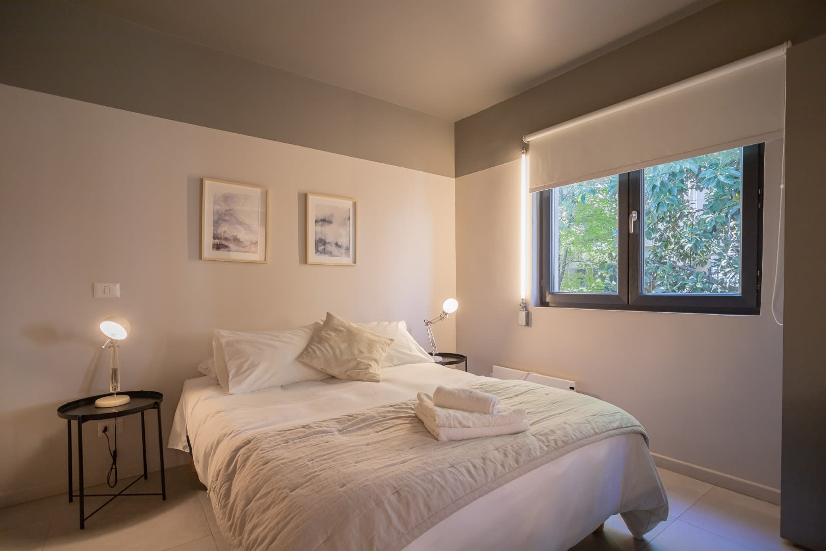 Relax in this serene bedroom with a cozy bed, soft lighting, and a refreshing view of lush greenery.
