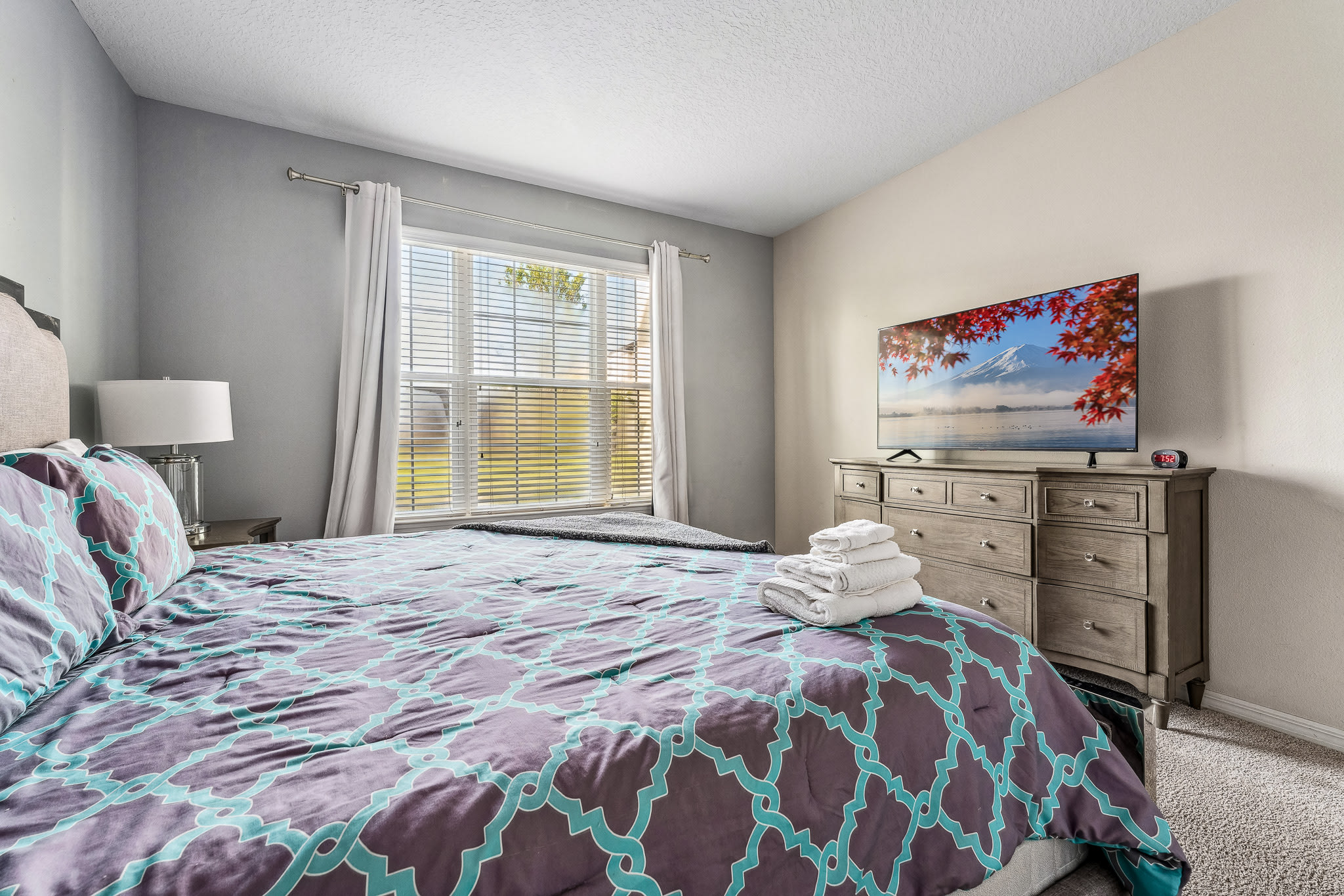 Comfortable bedroom w/ patterned bedding and a mounted TV.