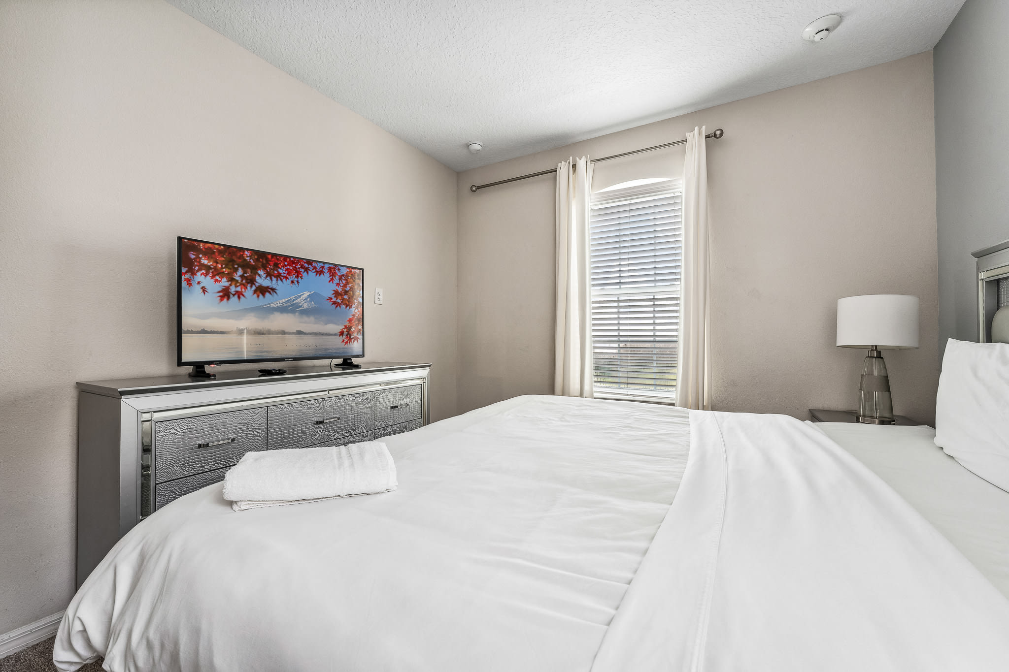Bright bedroom w/ crisp white bedding and a wall-mounted TV for easy unwinding.