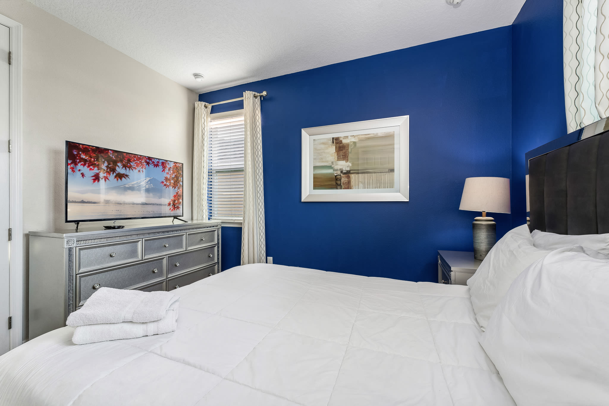 Clean, modern bedroom w/ white bedding and bright blue accent wall.
