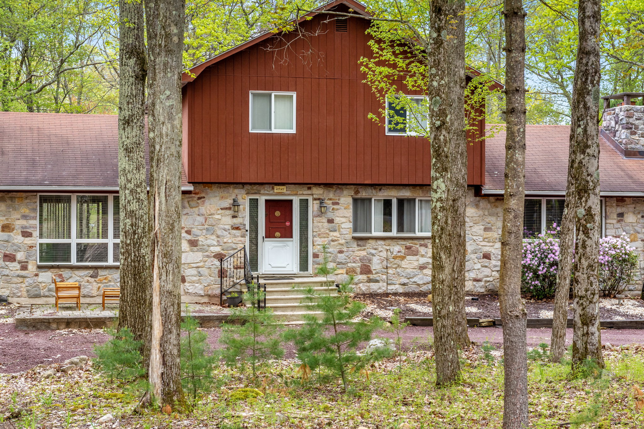 Nestled among tall trees, this charming home blends stone and wood elements, creating a warm and inviting exterior.