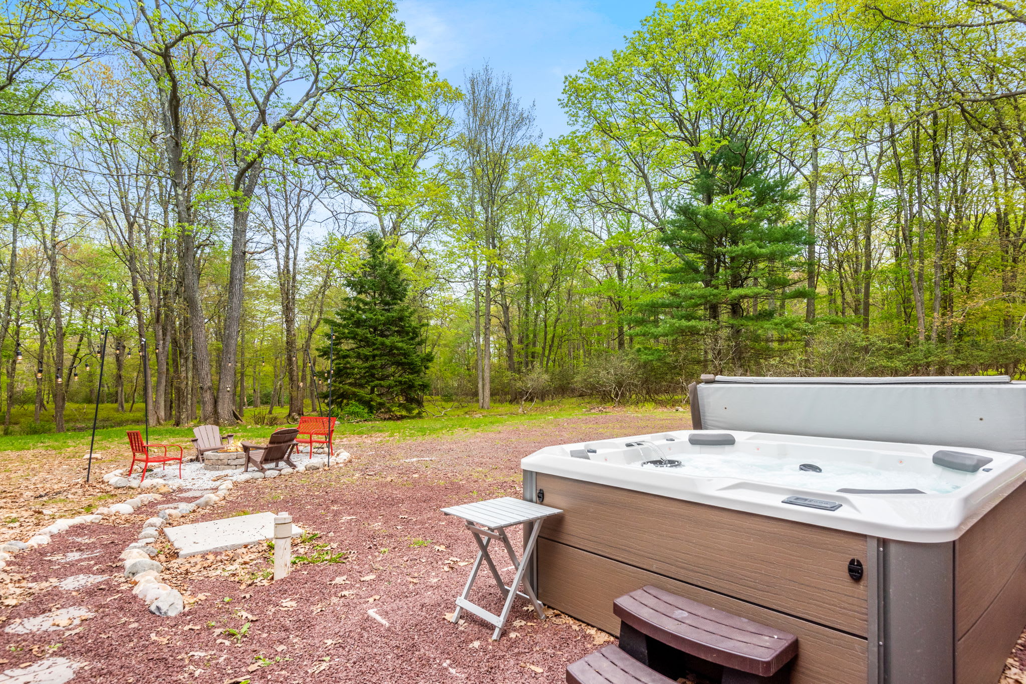 A serene backyard setting featuring a bubbling hot tub and a fire pit surrounded by Adirondack chairs. The perfect spot to unwind under the stars.