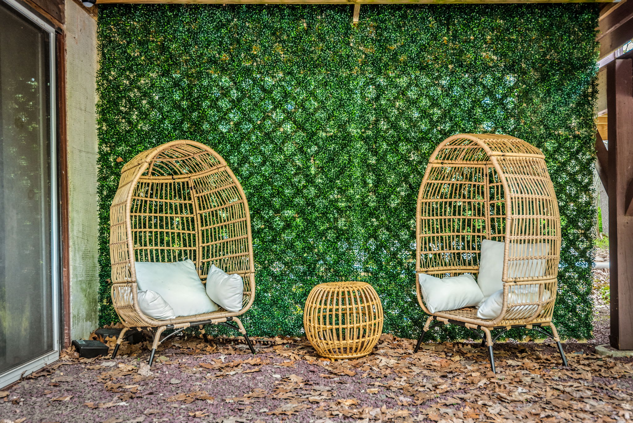 A cozy and stylish outdoor space featuring rattan egg chairs and a lush green wall, perfect for a peaceful retreat.