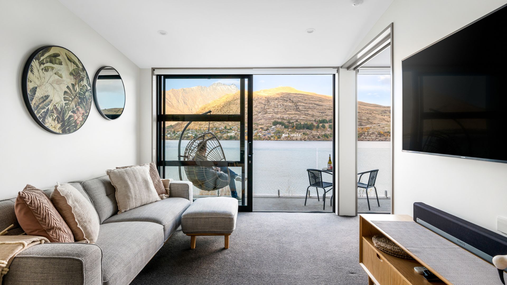 Stunning Lake and Mountain Views – Relax in this inviting living room, featuring a large flat-screen TV and expansive windows that showcase panoramic views of the lake and mountains, perfect for unwinding after a day of exploration.