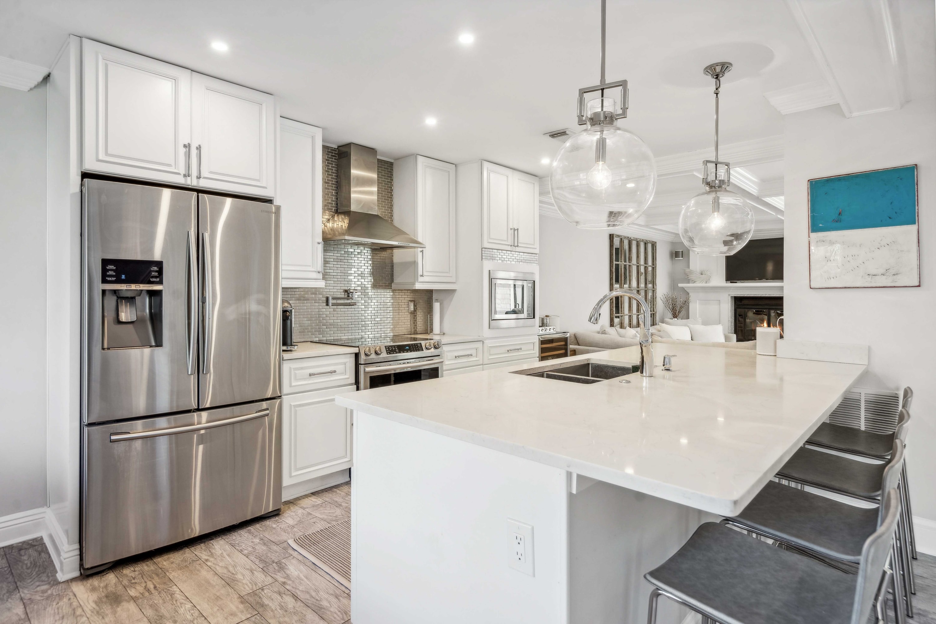 Kitchen with a white island, quartz countertops, stainless refrigerator, and globe pendant lights.
