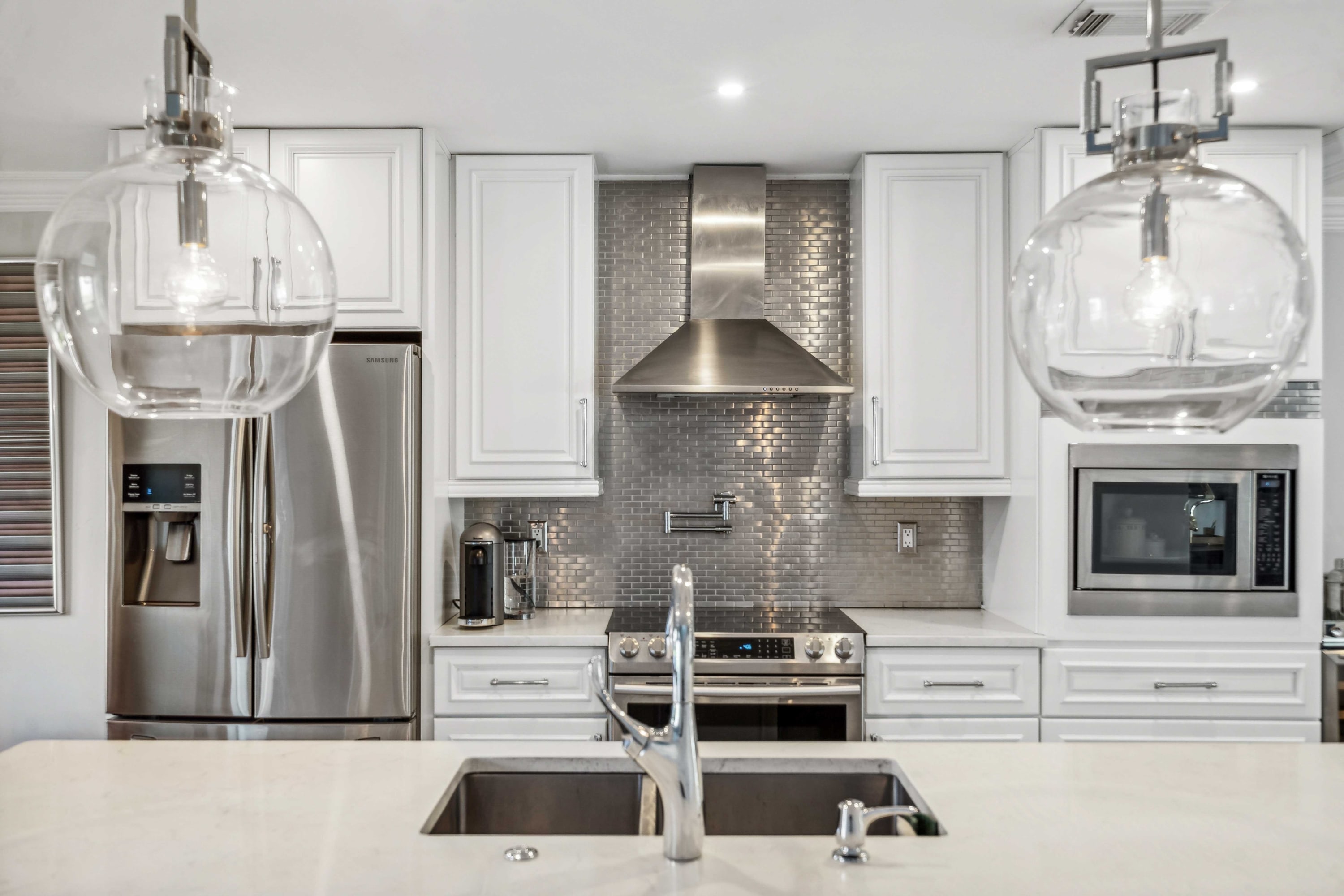 Kitchen detail with a farmhouse sink, gas range, subway-tile backsplash, and glass pendant lighting.
