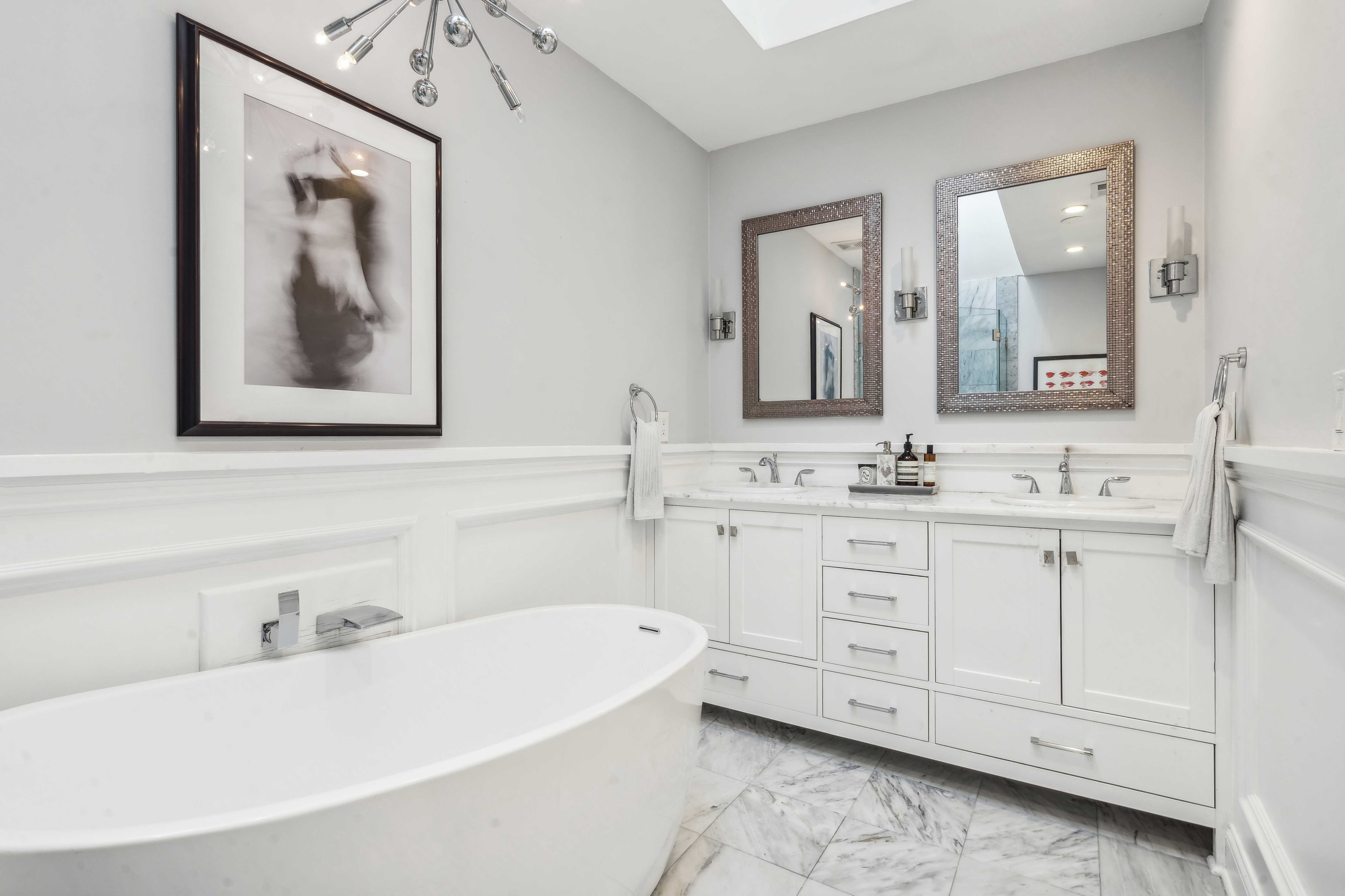 Bathroom with a freestanding soaking tub, double vanity, and marble-tiled walls.