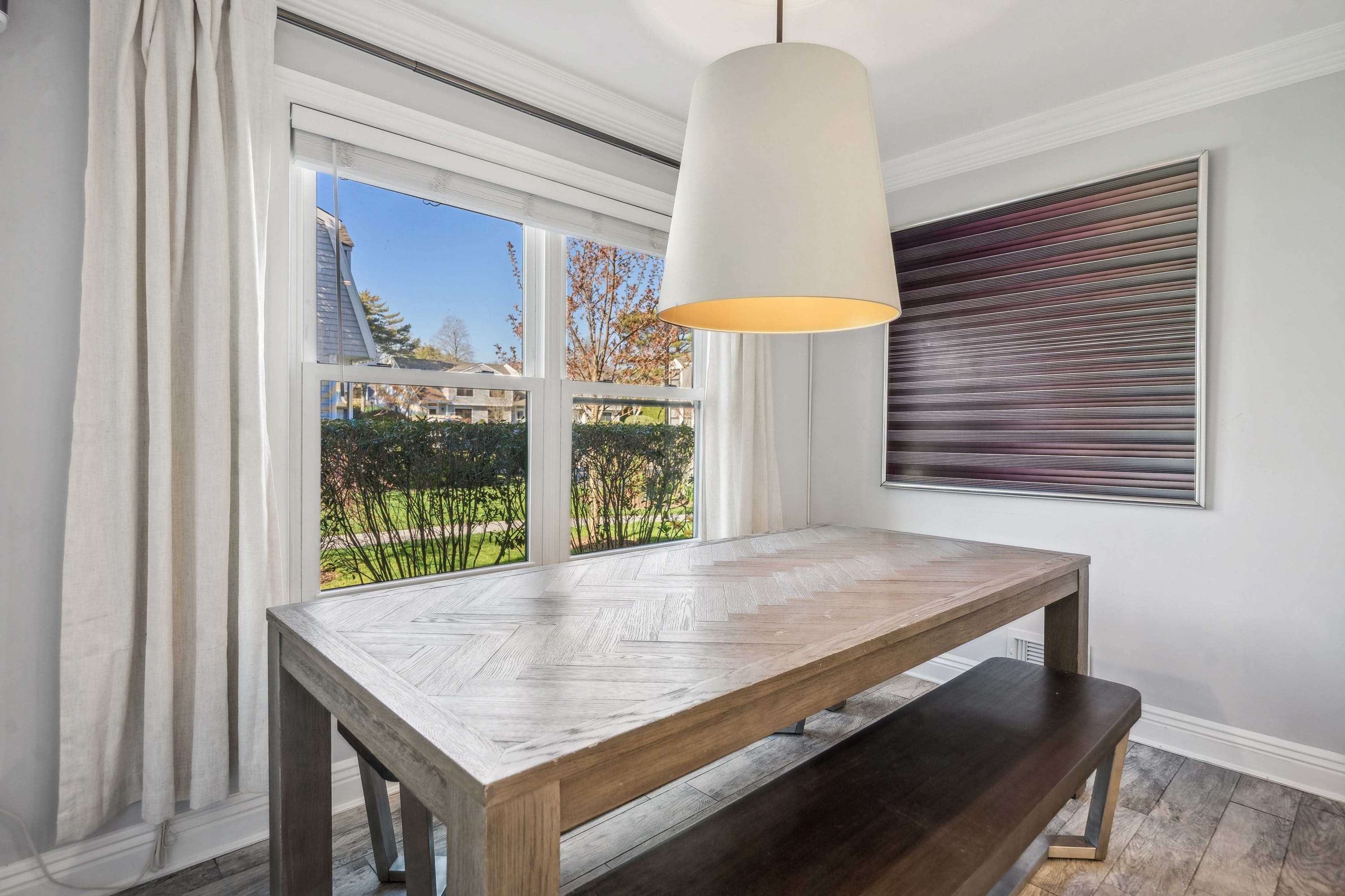 Breakfast nook table and bench beneath a linen pendant shade, with a garden-view window.
