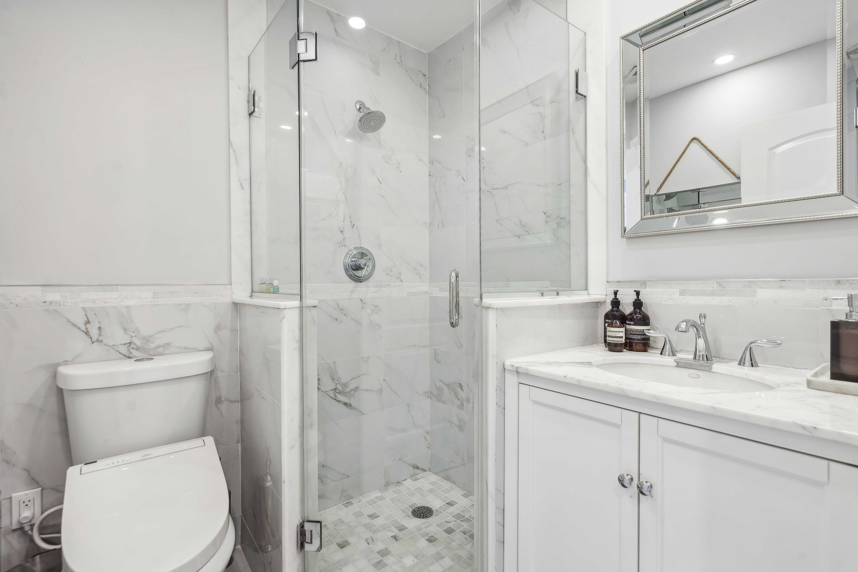 Bathroom with a glass-enclosed marble shower and a stone-topped vanity.