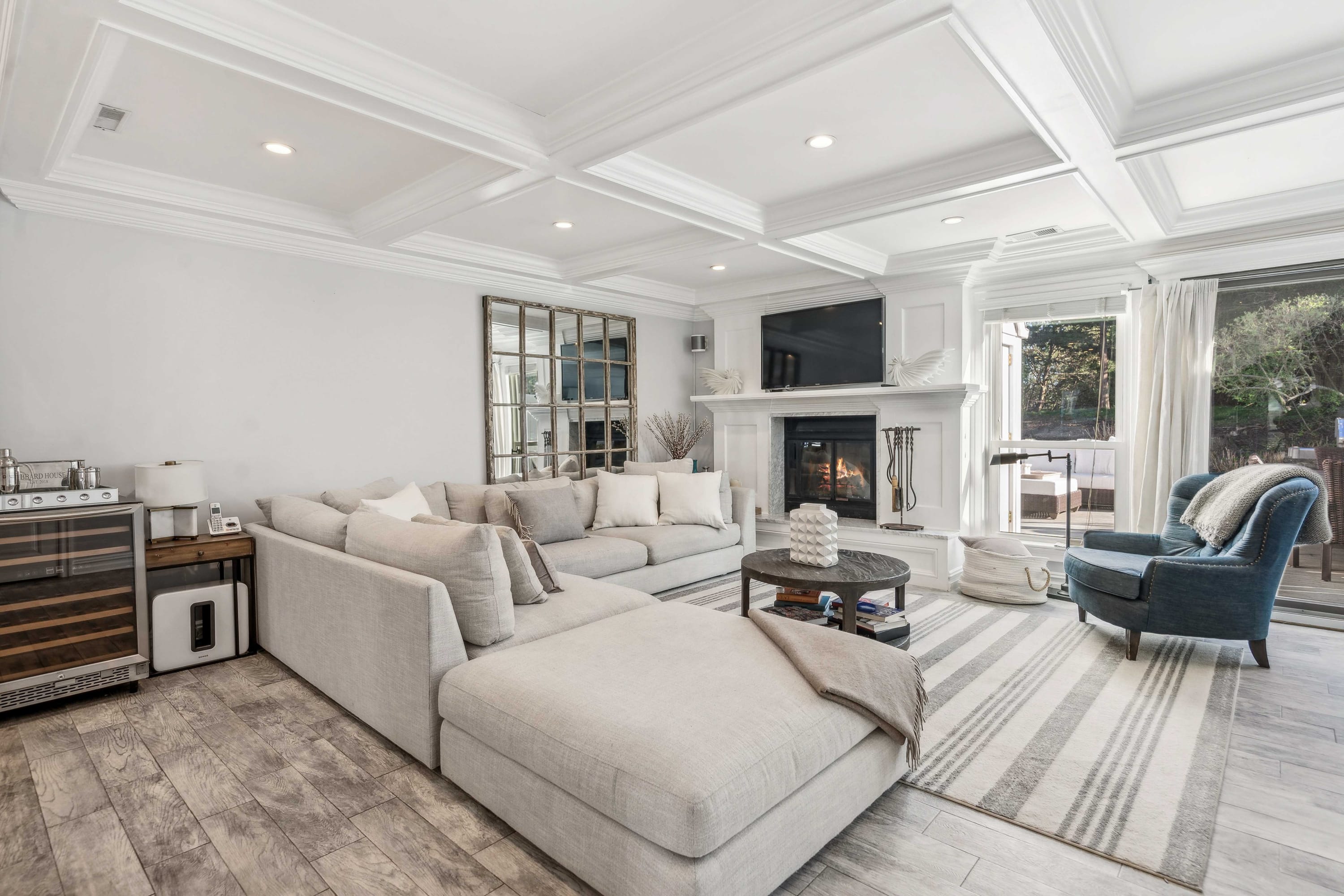 Living room with a gray sectional sofa, fireplace, mirrored wall, and coffered ceiling.