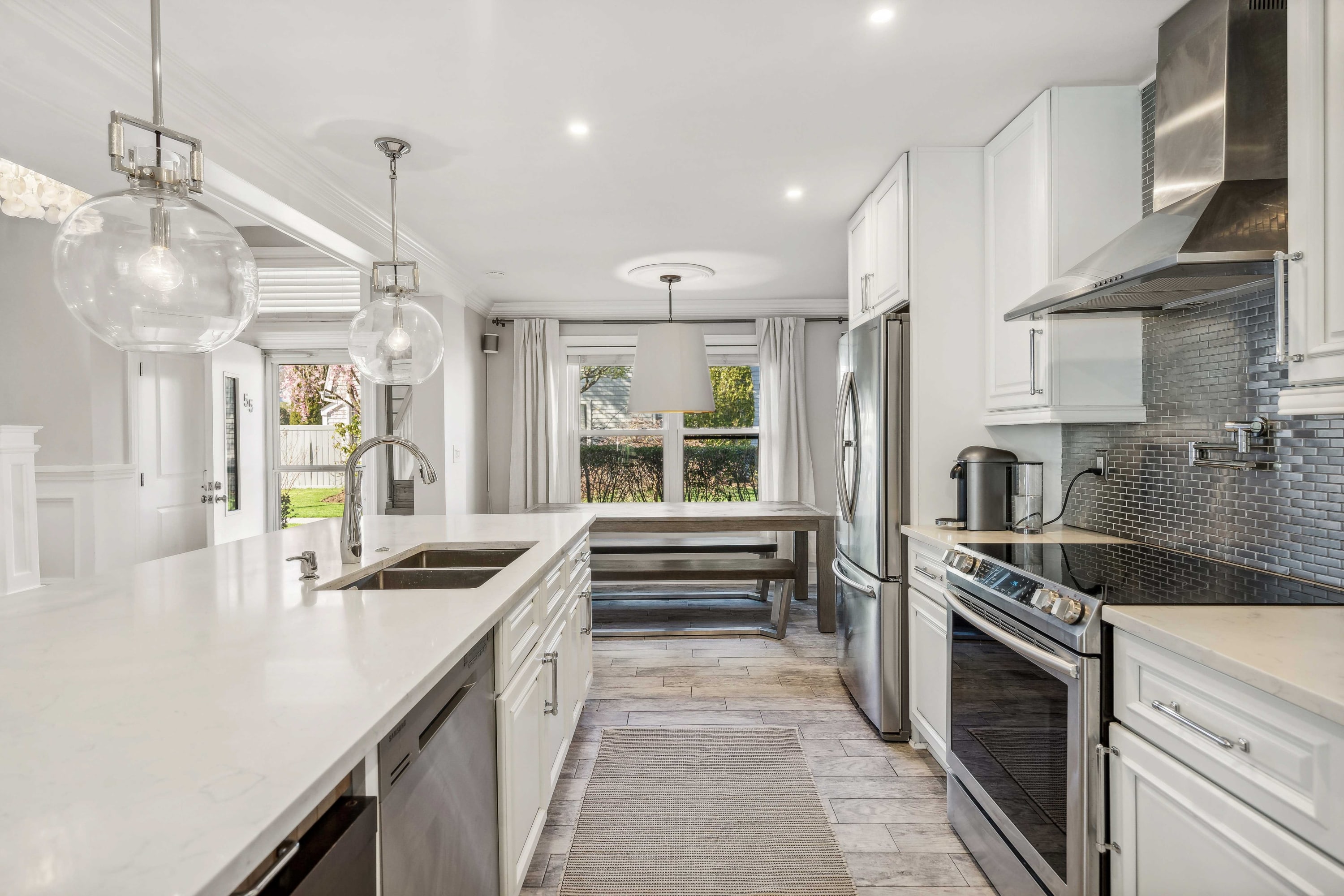 Kitchen island view down a hallway toward the dining area, with white cabinetry and wood-look flooring.