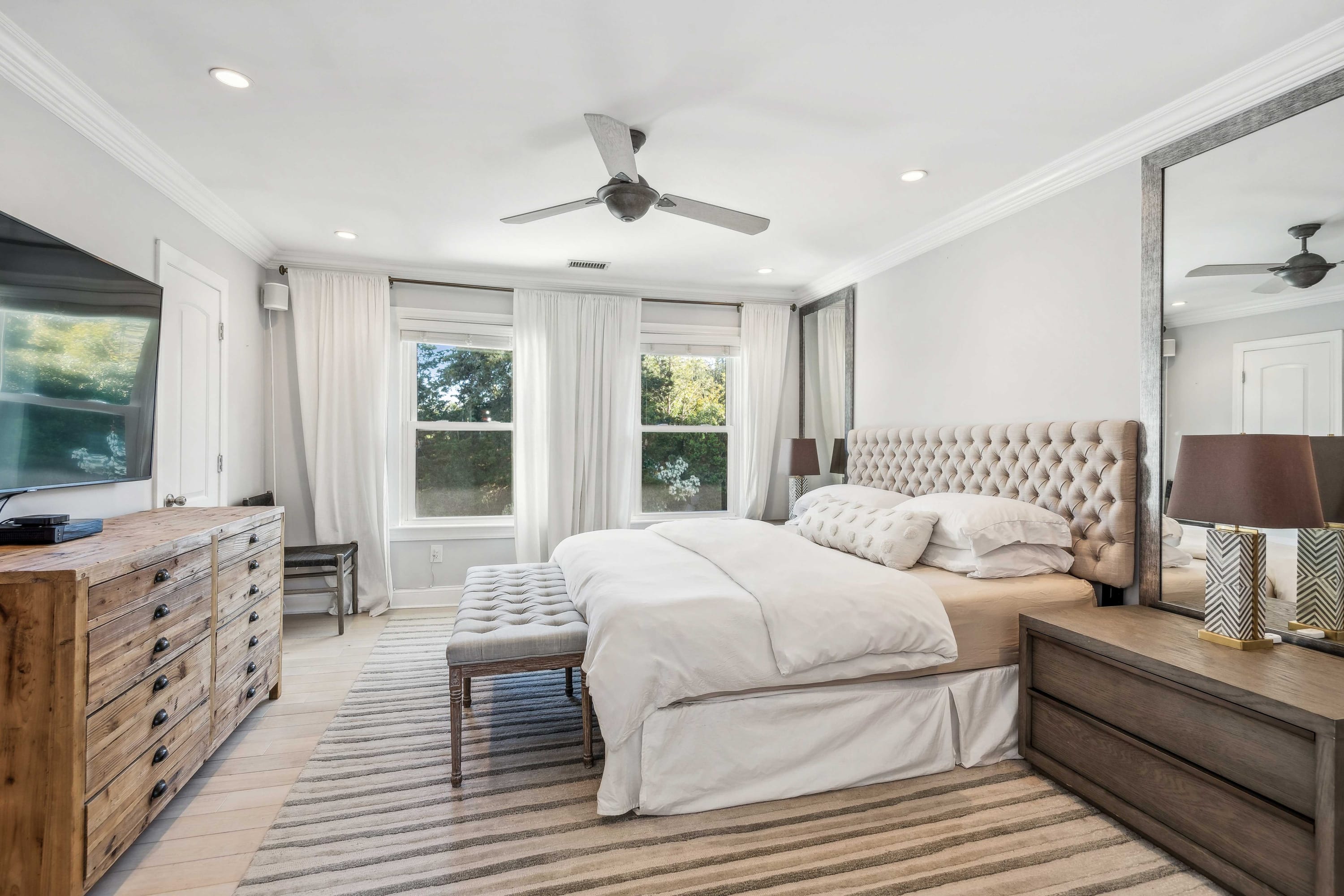 Bedroom with a tufted upholstered headboard, wood dresser, and wall-mounted TV.