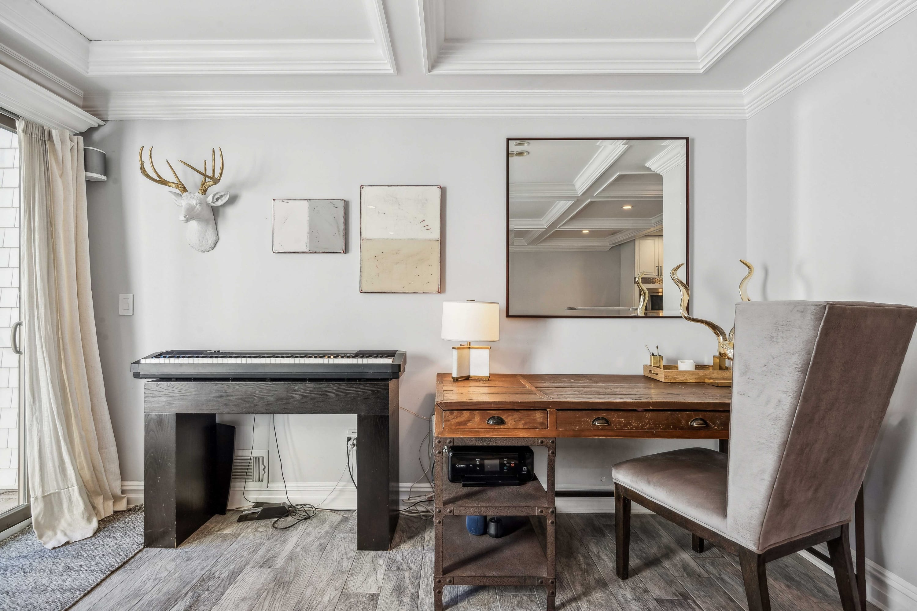 Den with a mounted deer-head decor piece, wood writing desk, and decorative mirror.