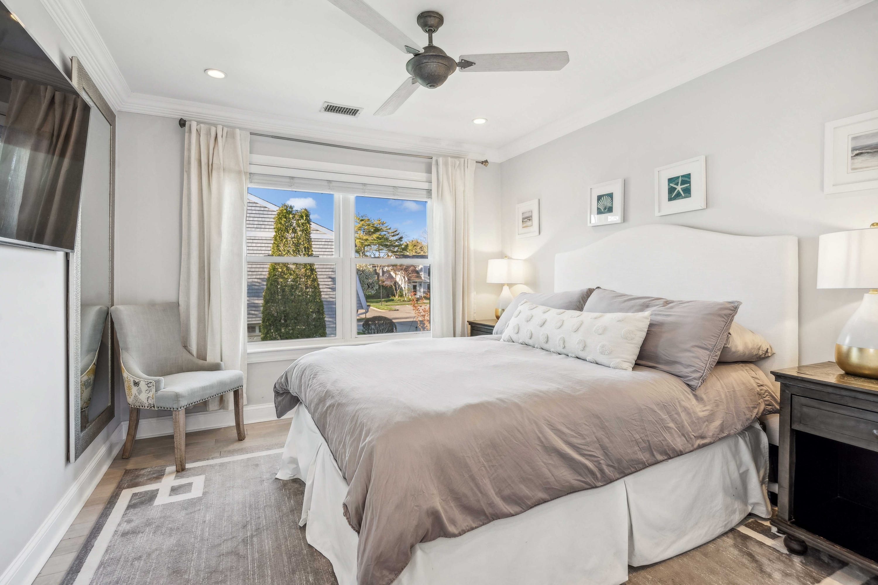 Bedroom with a tufted headboard, ceiling fan, and windows overlooking the neighborhood.