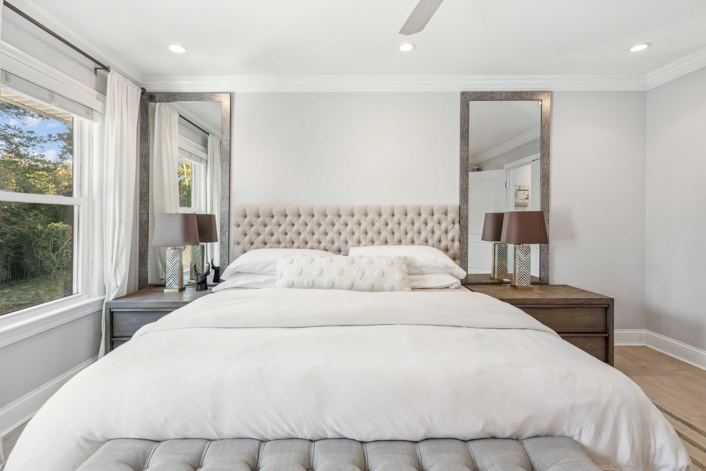 Bedroom with a tufted headboard, dark wood nightstands, and full-length mirror.