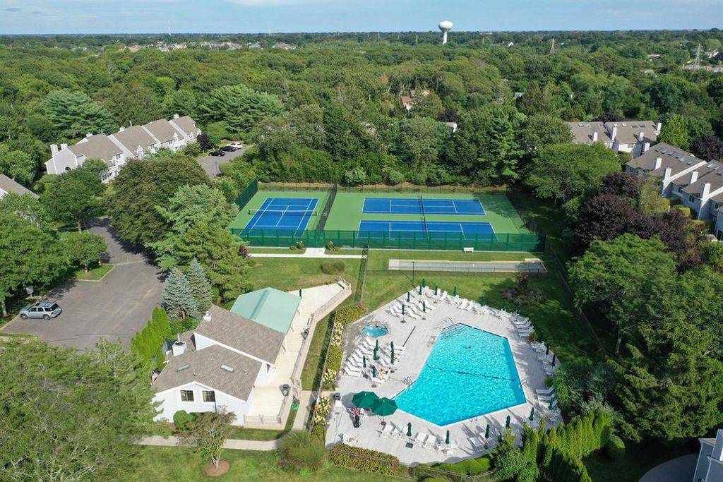 Aerial view of the community's pool, tennis courts, and clubhouse amid wooded grounds.