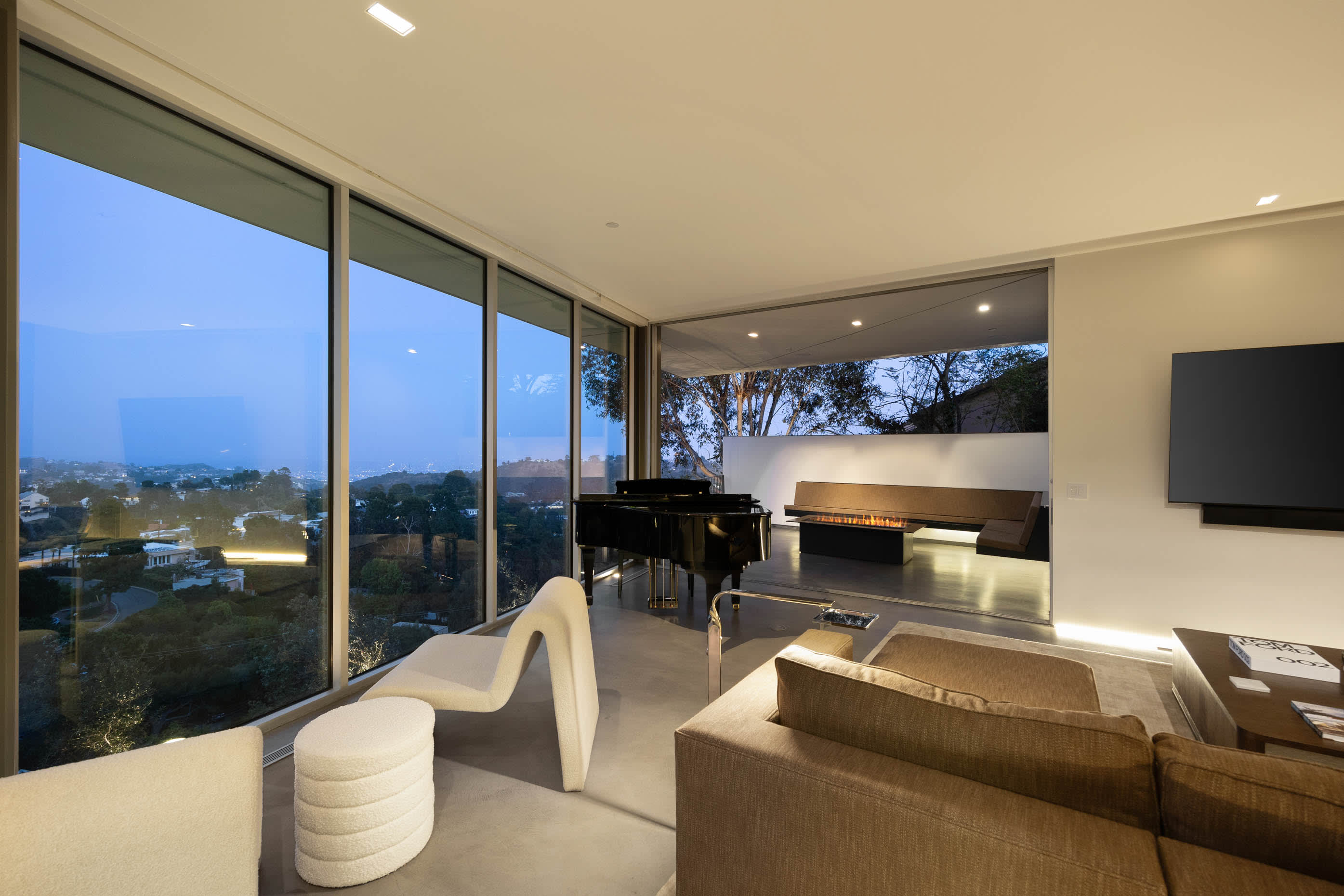 Living space with a grand piano, fire pit, and stunning night sky city views.