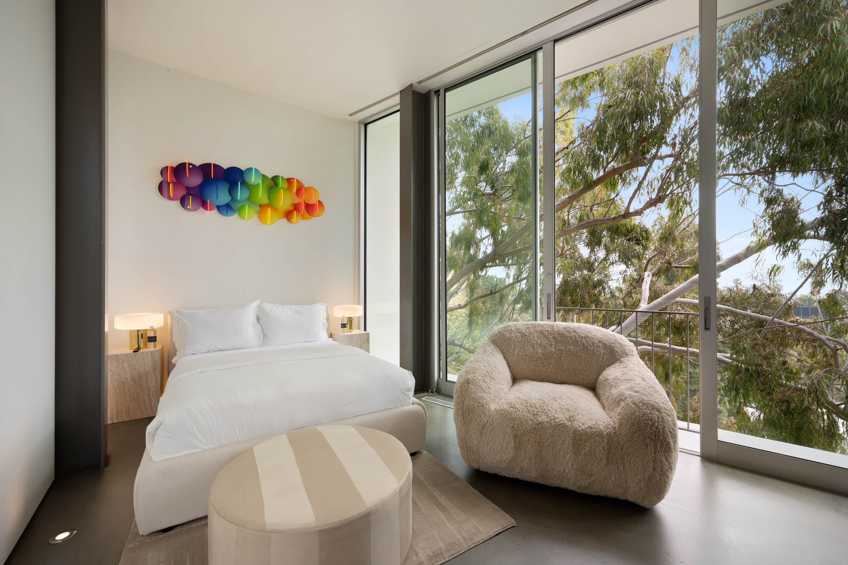 Bedroom with floor-to-ceiling glass doors opening to nature, complemented by modern amenities .