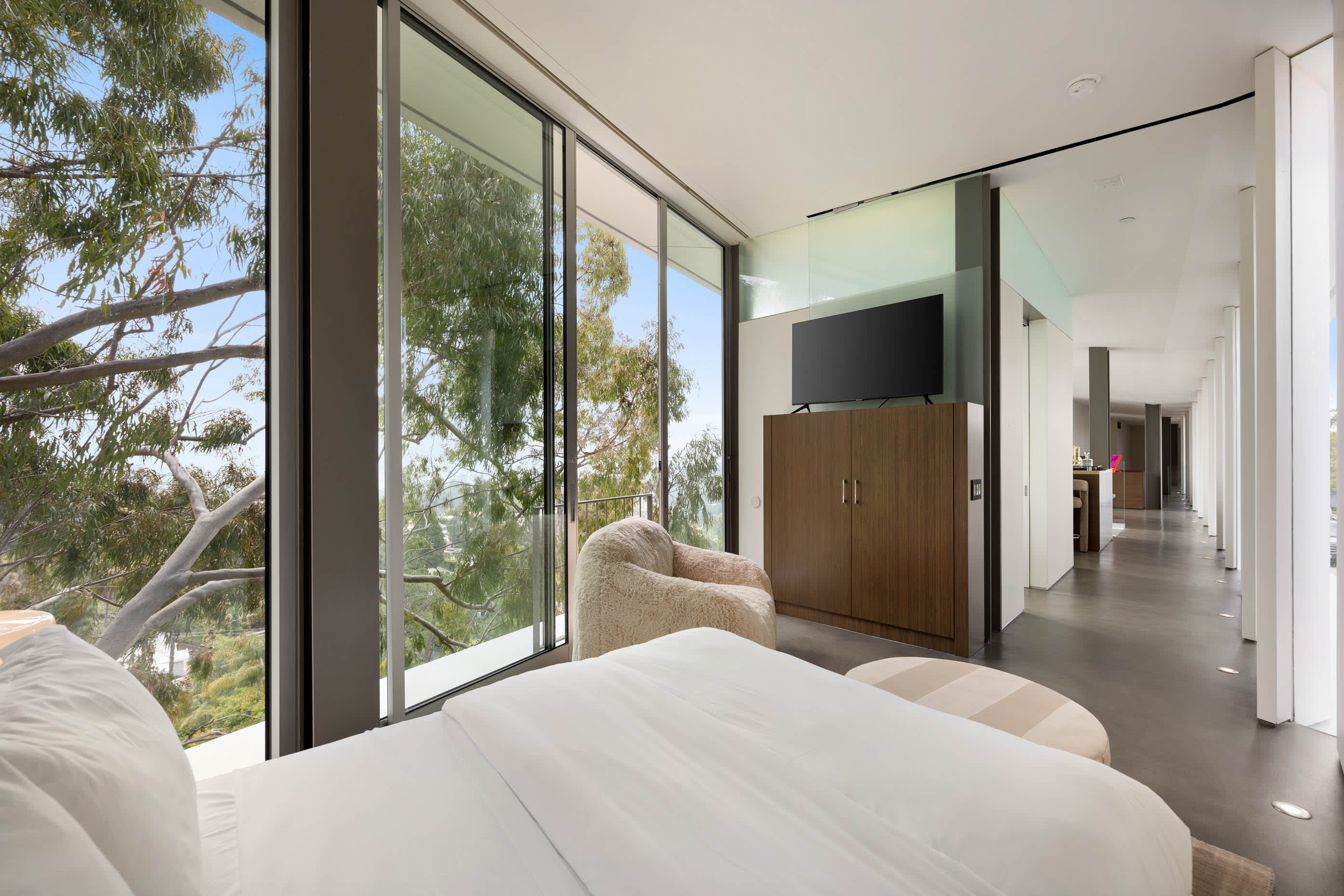 Luxurious bedroom with floor-to-ceiling glass doors opening to nature, designed for comfort and relaxation with modern amenities.