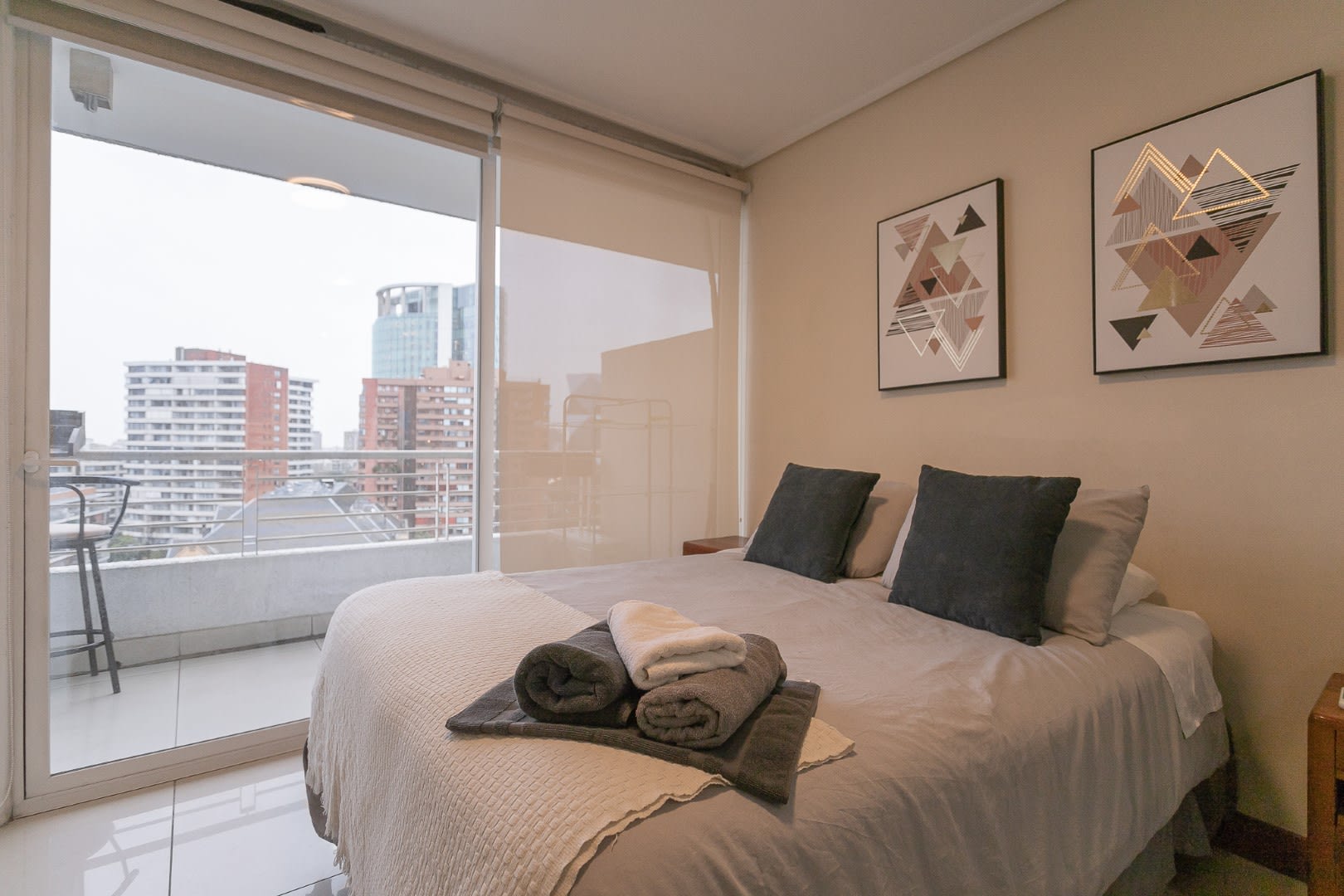 Cozy bedroom with plush bedding and a private balcony offering stunning city views, perfect for relaxation.