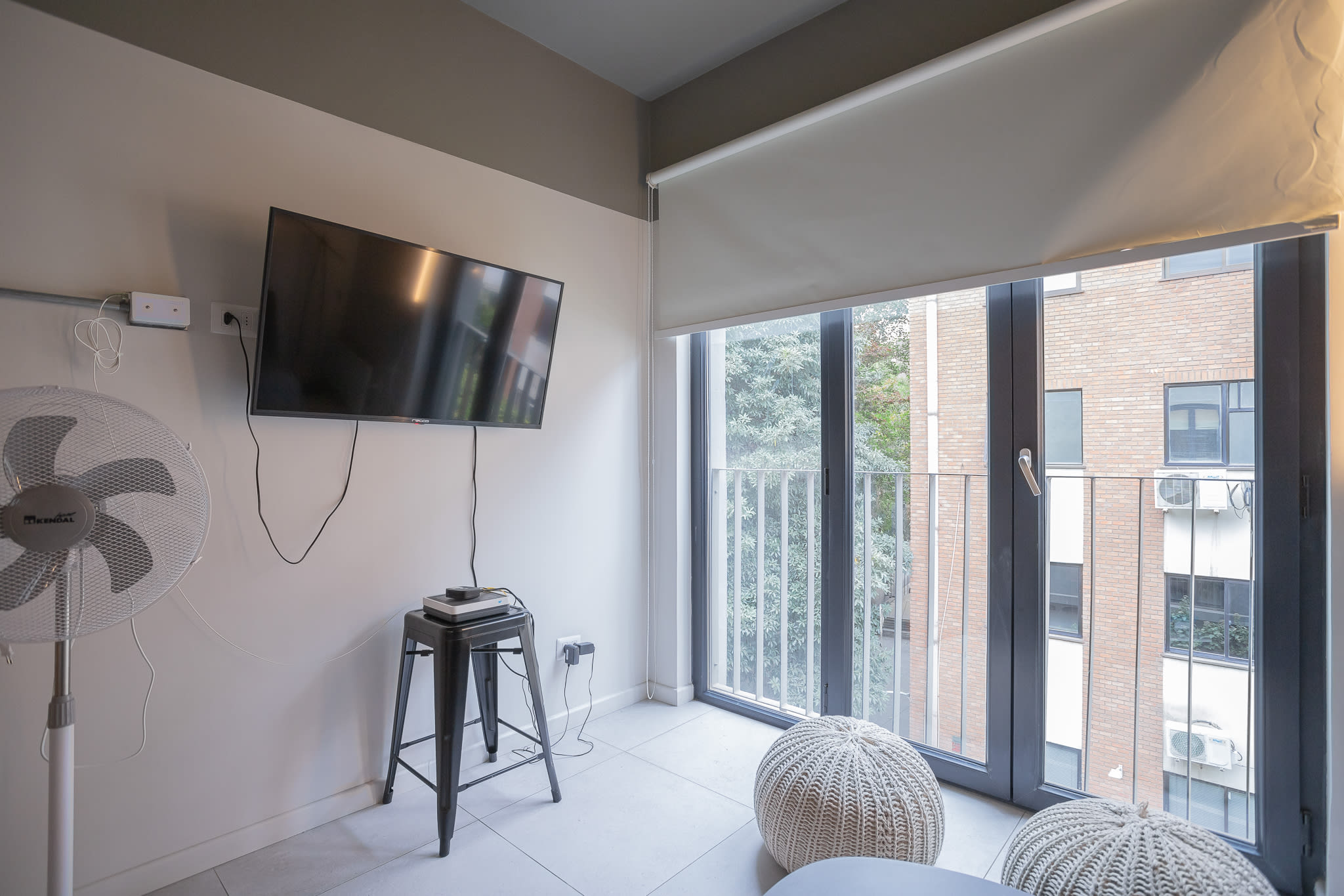 Bright and airy living space with a wall-mounted TV and large windows offering a charming view, perfect for relaxation.