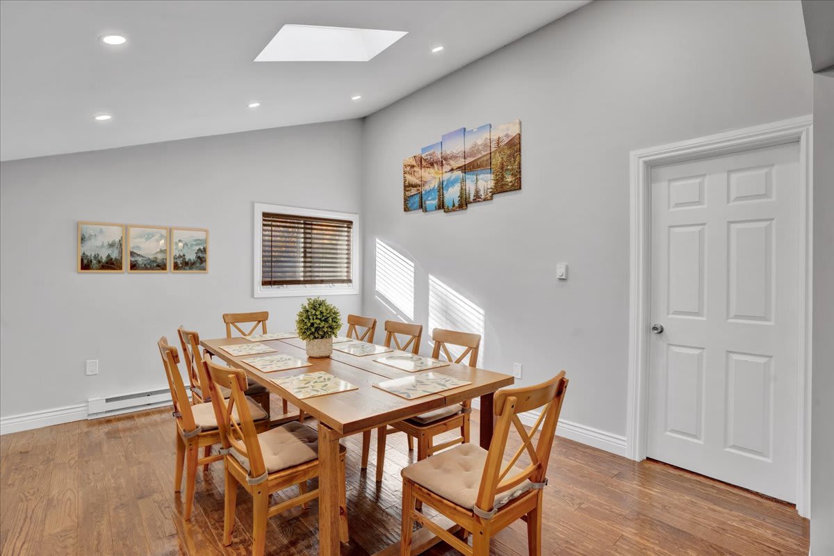 A long wooden dining table with natural wood chairs creates a welcoming atmosphere for shared meals. The skylights above enhance the bright and fresh feel of the space.
