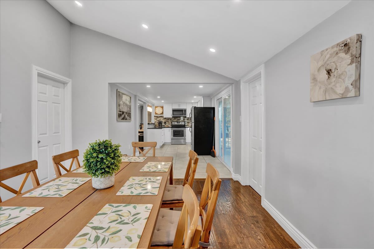 A spacious wooden dining table with stylish chairs sits under bright recessed lighting, making it perfect for gatherings.