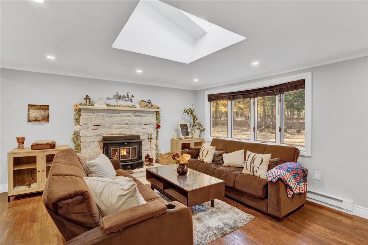 A stone fireplace adds warmth, complemented by plush brown sofas and a cozy neutral color palette. The skylights flood the space with natural light, making it feel open and airy.