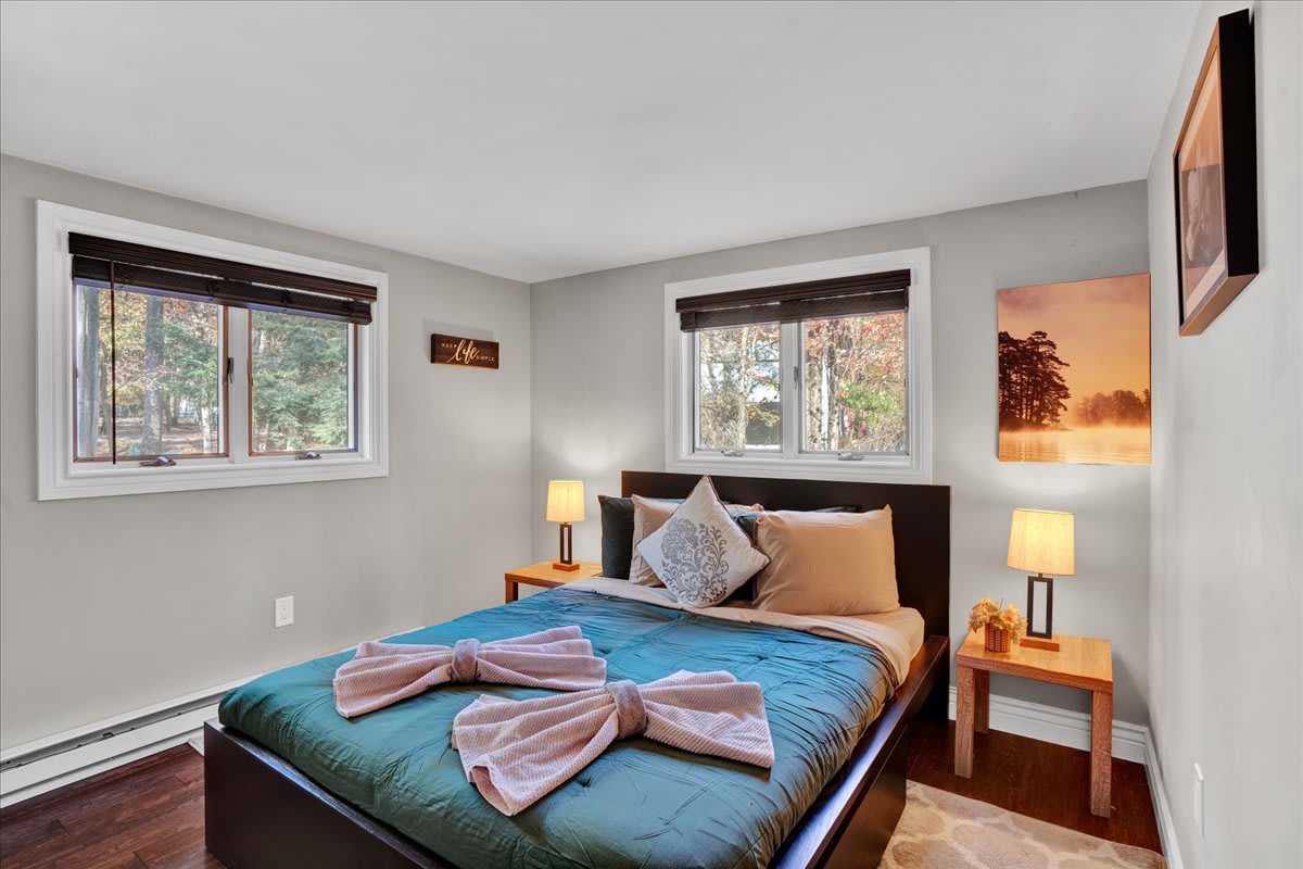 This serene bedroom offers a comfortable bed with fresh linens and soft lighting. Wake up to peaceful woodland views from the large windows, setting the perfect tone for a restful stay.