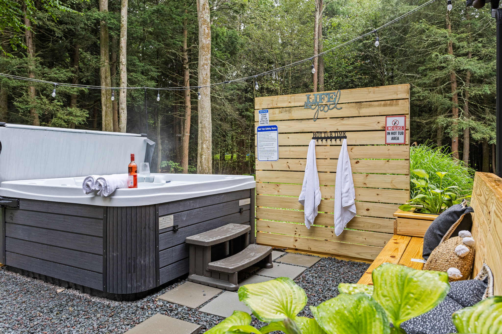 Serene Outdoor Hot Tub Retreat – A private and relaxing hot tub setup surrounded by lush greenery, complete with a stylish wooden privacy wall and cozy seating.