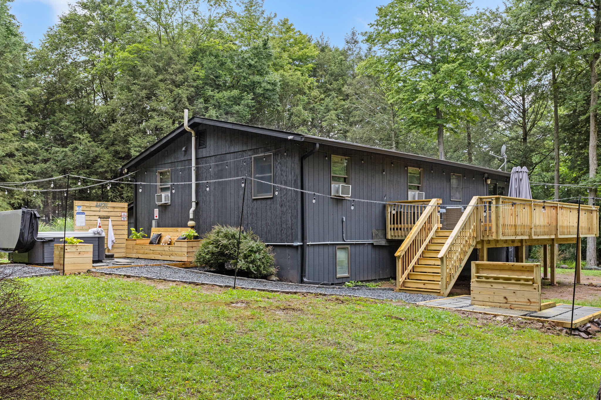 Chic Modern Cabin Exterior – A stylish black cabin nestled in nature, featuring a spacious deck and a large yard for outdoor activities.