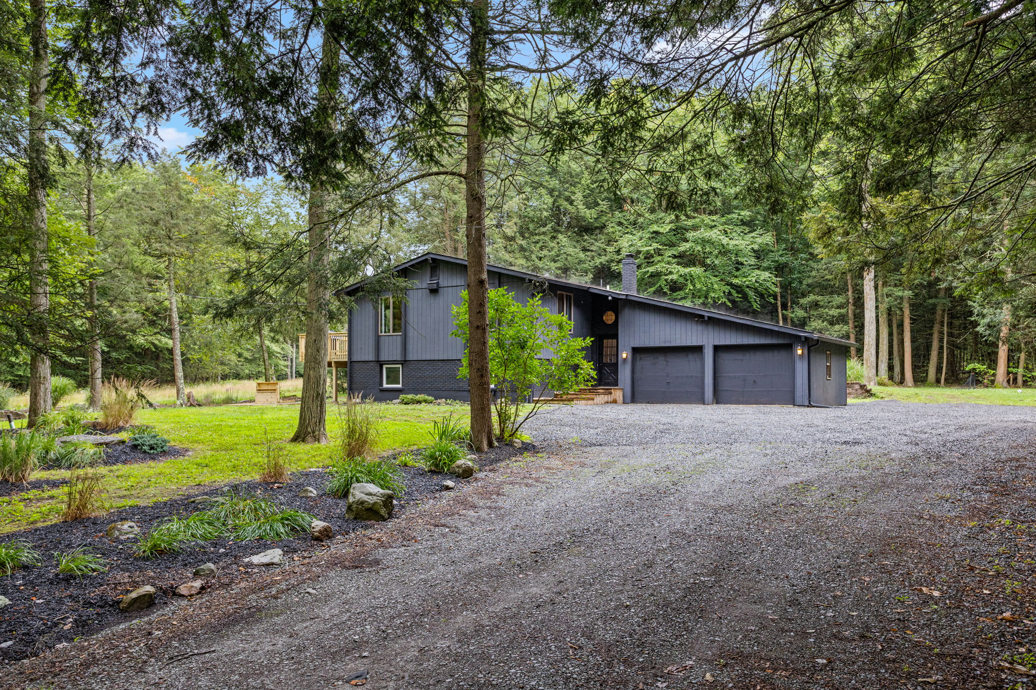 Secluded Modern Cabin Escape – A stylish black cabin nestled among the trees, offering a private retreat with a spacious driveway and lush natural surroundings.
