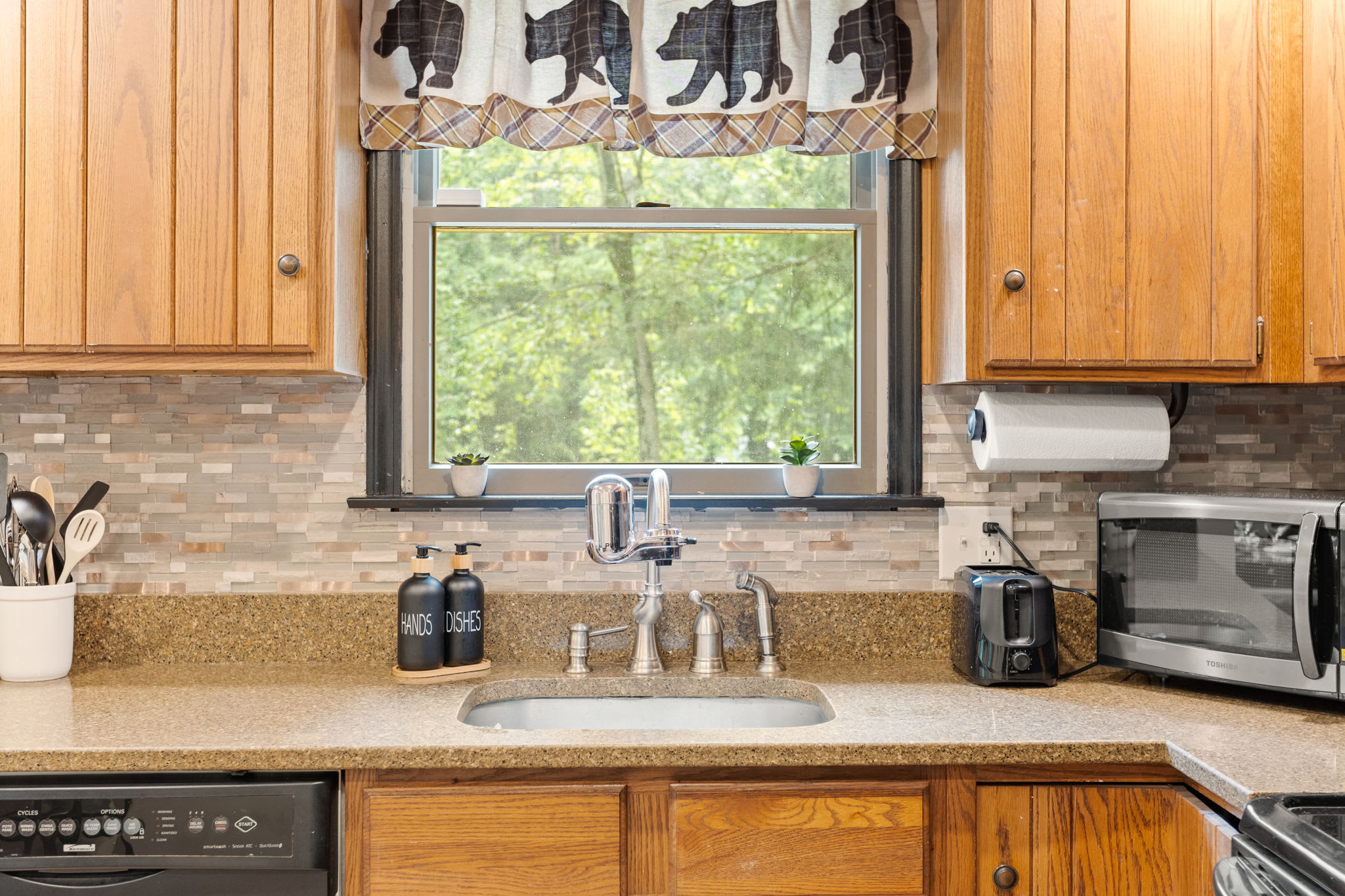 Bright & Functional Kitchen Space – A large kitchen window allows natural light to flow in, highlighting the rustic wood cabinetry and a well-organized cooking space.