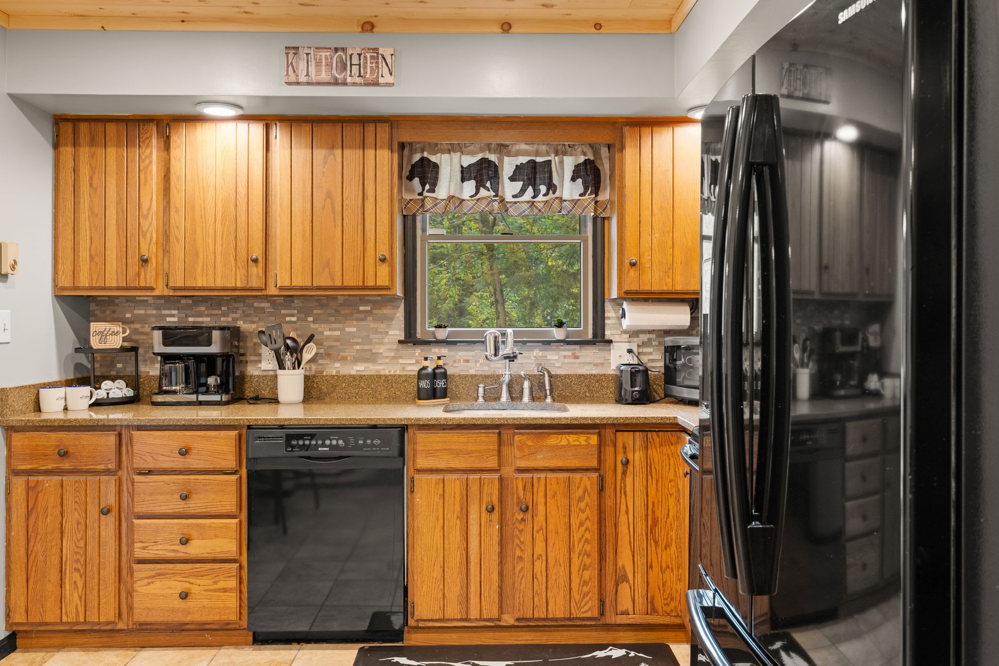 Classic & Cozy Cabin Kitchen – A warm and inviting kitchen with wooden cabinetry, black appliances, and a charming window view that enhances the rustic feel.