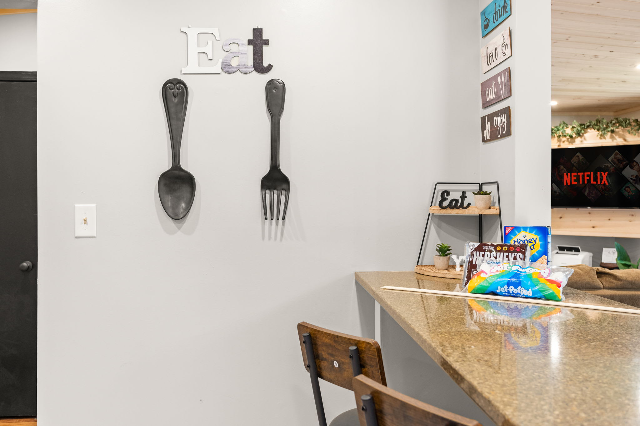 Playful & Cozy Kitchen Wall Decor – Oversized fork and spoon wall art add a fun touch to the dining space, complementing the inviting kitchen bar setup.