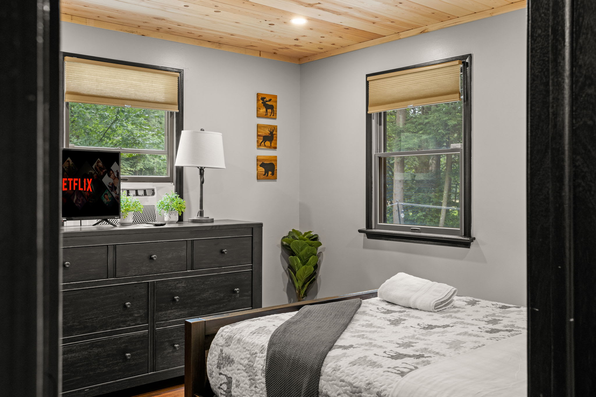 A stylish bedroom featuring a dark wood dresser, warm lighting, and large windows that bring in plenty of natural light.