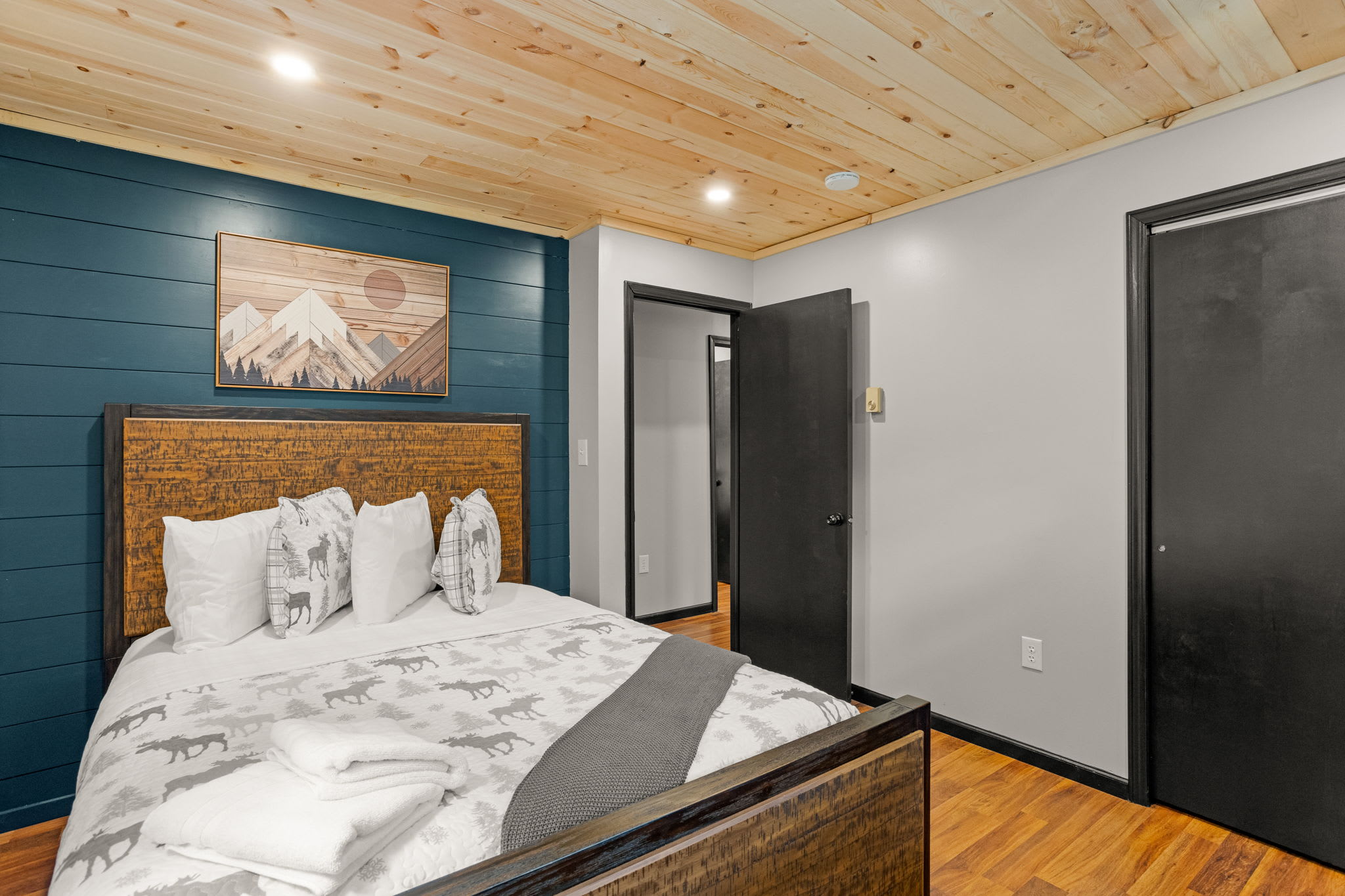 Cozy & Contemporary Third Bedroom – A stylish sleeping space with a bold blue accent wall, warm wood ceiling, and plush bedding for a restful stay.