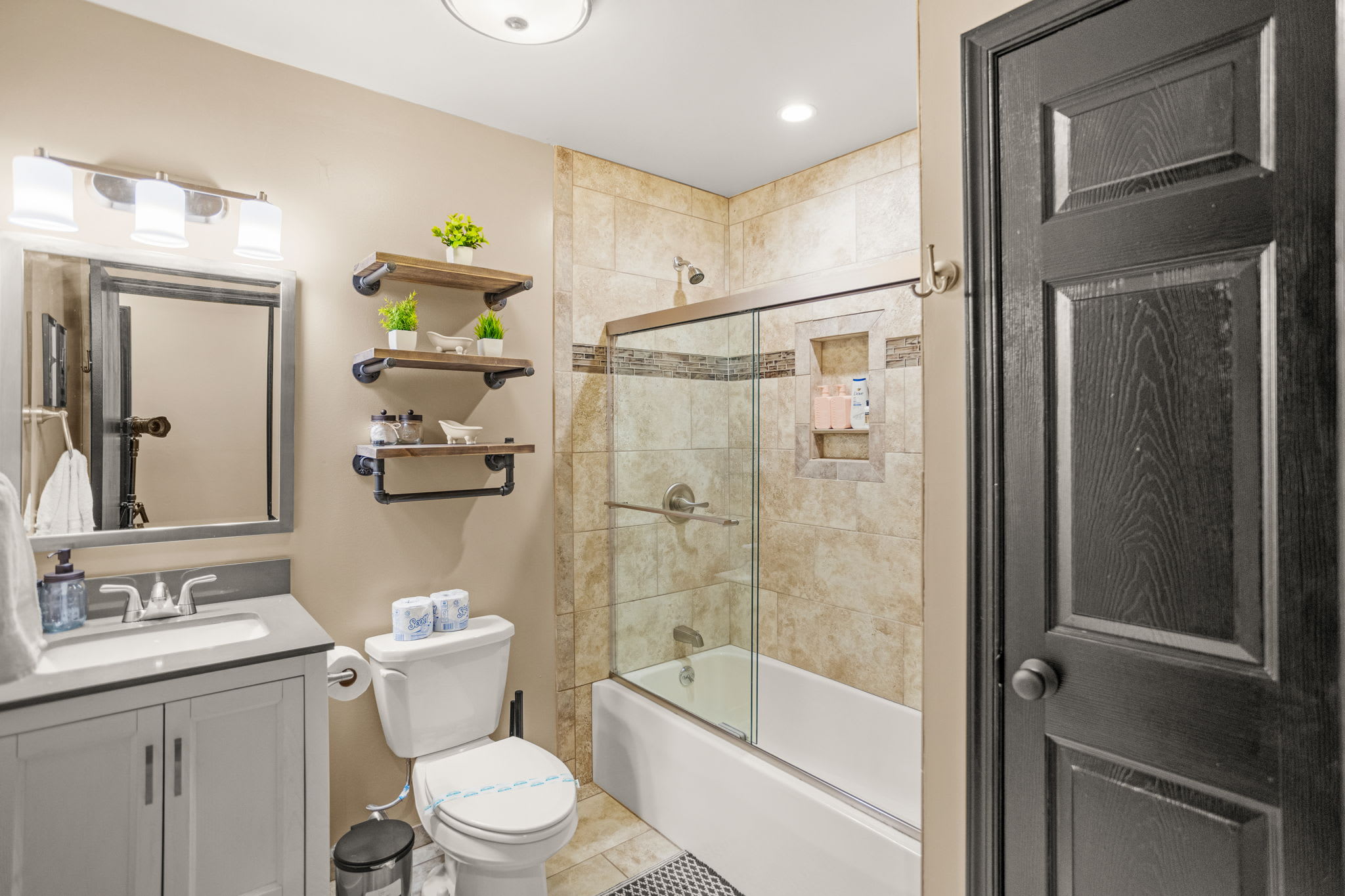 A well-lit bathroom featuring a chic blend of modern fixtures, floating shelves, and warm tile accents.
