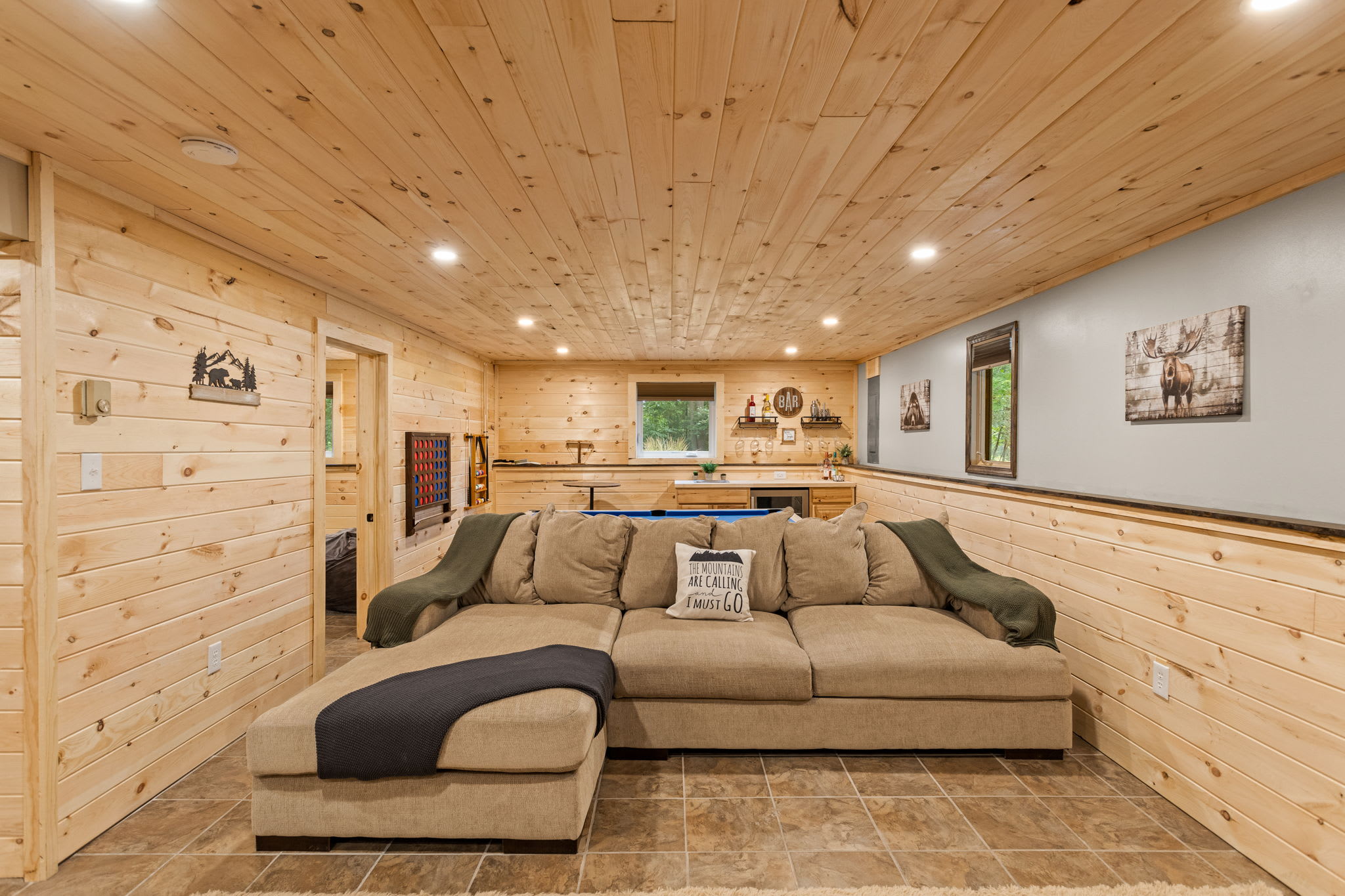 A spacious and well-lit lounge area with a large sectional sofa, wood paneling, and decor that enhances the cozy cabin feel.