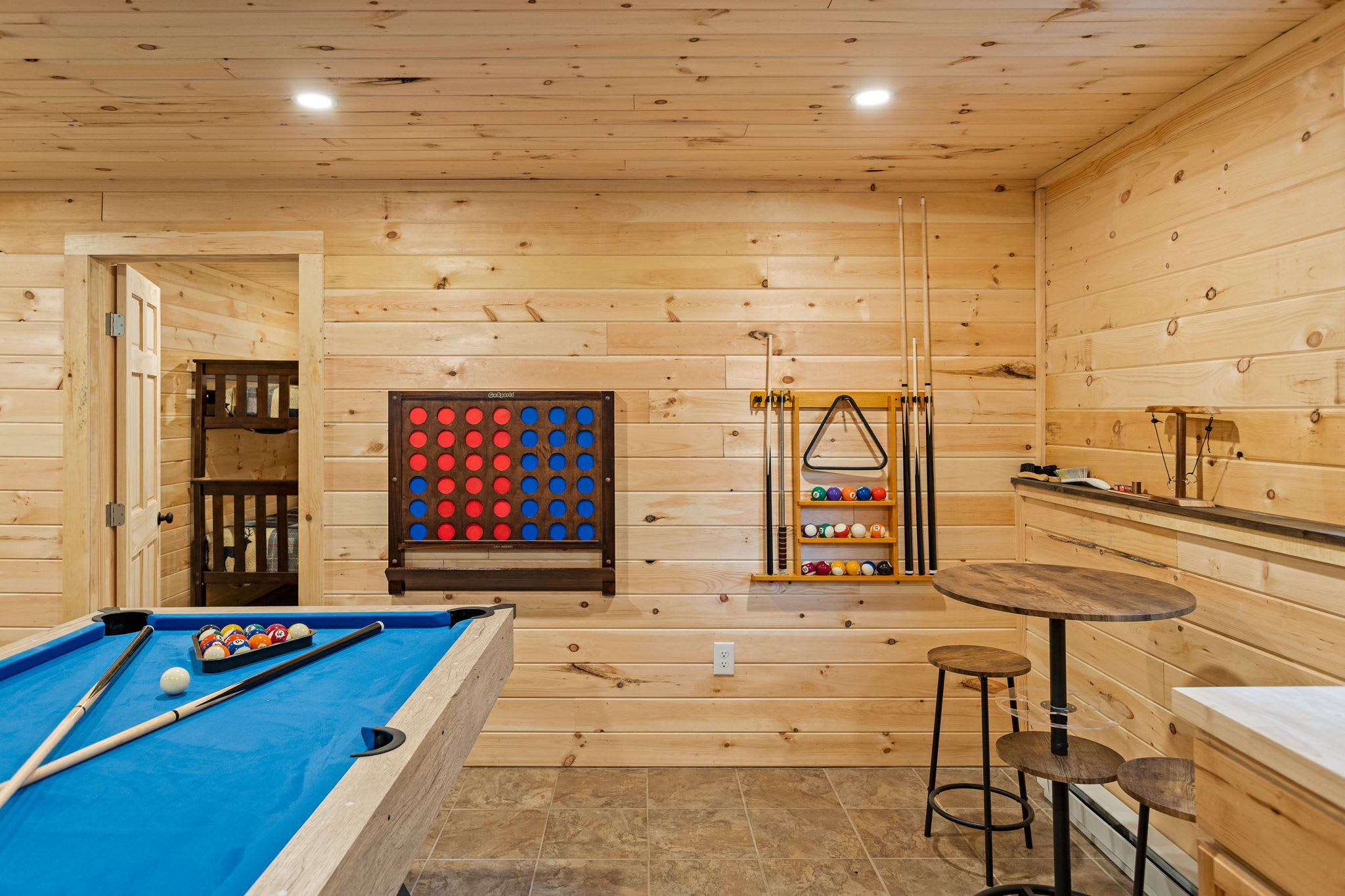 A beautifully designed entertainment space featuring a pool table, oversized wall-mounted Connect Four, and warm wood-paneled walls.
