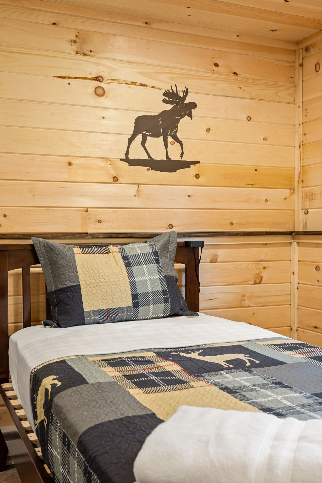 A charming and cozy sleeping space featuring a moose wall decal, warm wood walls, and soft plaid bedding for a mountain-inspired retreat.