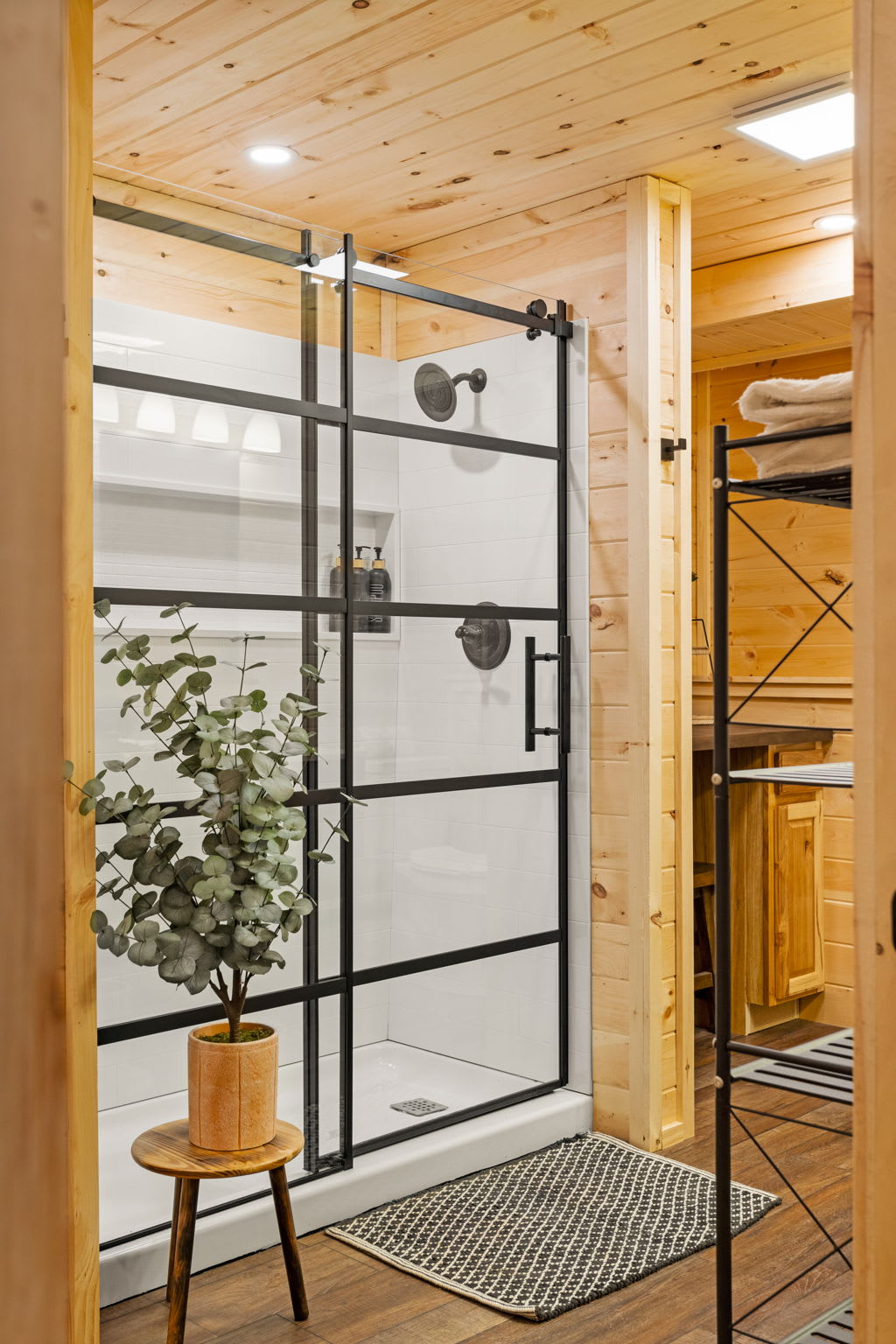 Rustic Walk-In Shower Retreat – A stunning glass-enclosed shower with a sleek black frame, warm wood paneling, and greenery for a spa-like touch.